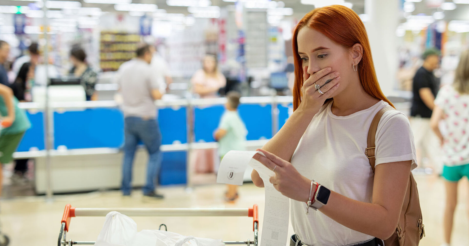 Überraschte Frau betrachtet die Einkaufs-Rechnung im Supermarkt
