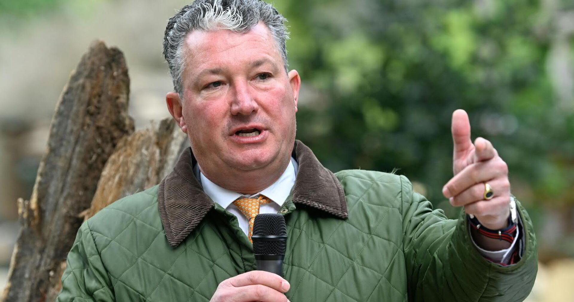 Ein Mann mit einer grünen Jacke spricht in ein Mikrophon.