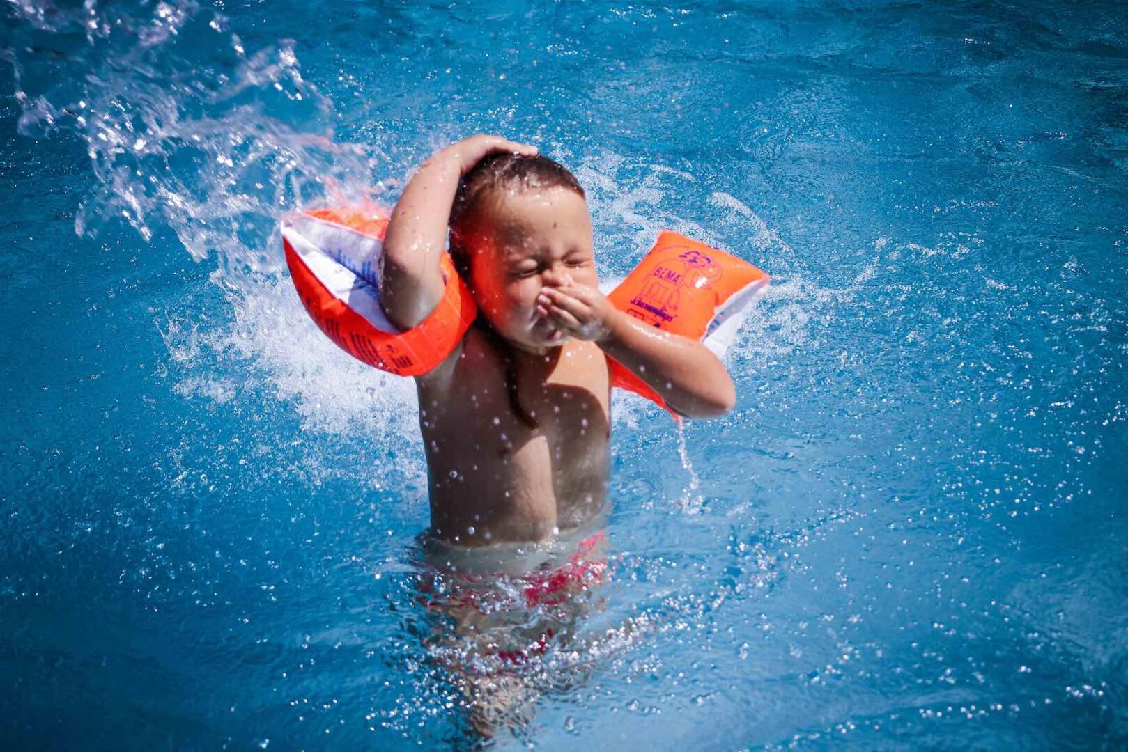 Kleinkind mit orangen &quot;Schwimm-Flügerln&quot; im Becken.