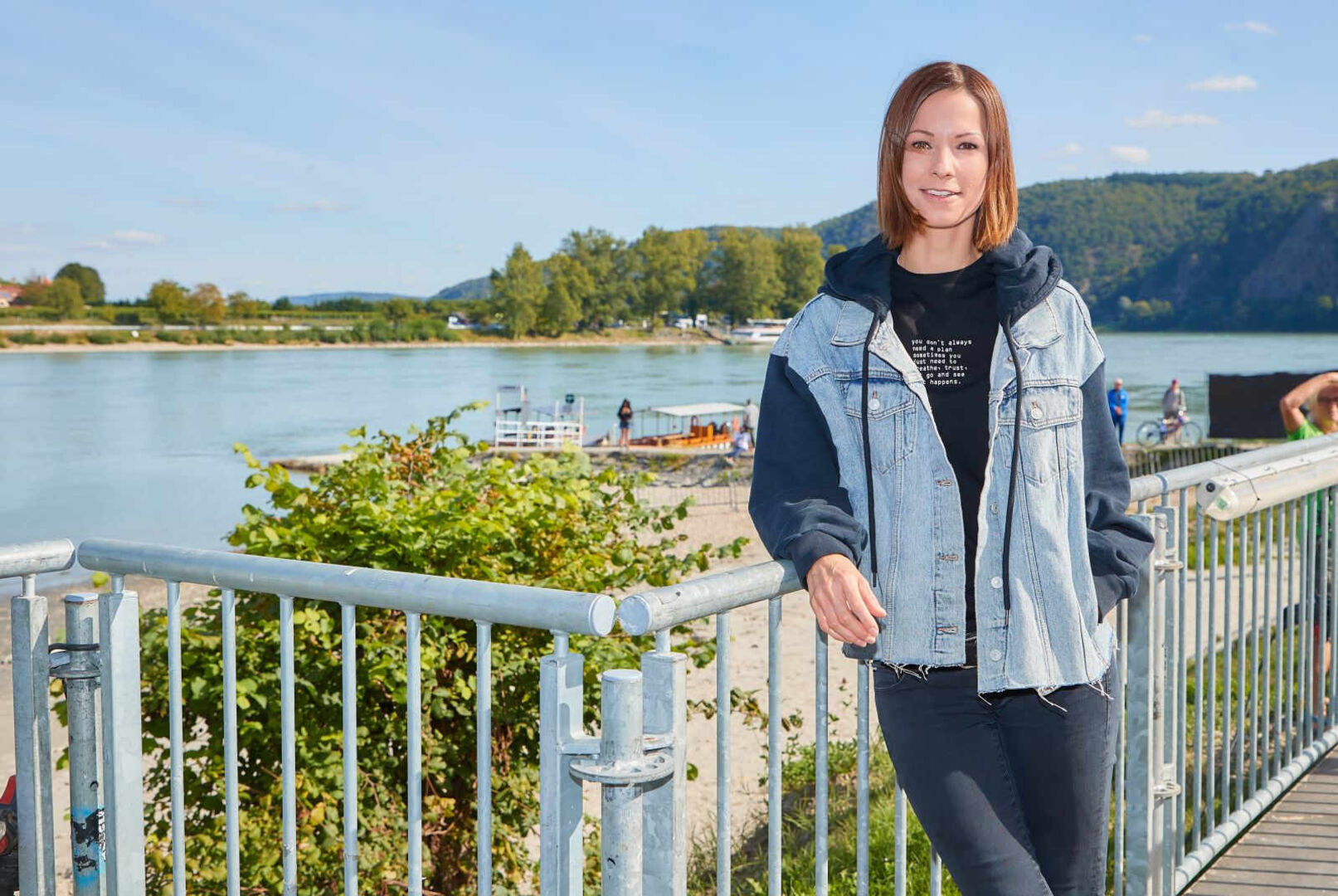 Christina Stürmer vor einem Fluss mit Jeansjacke.