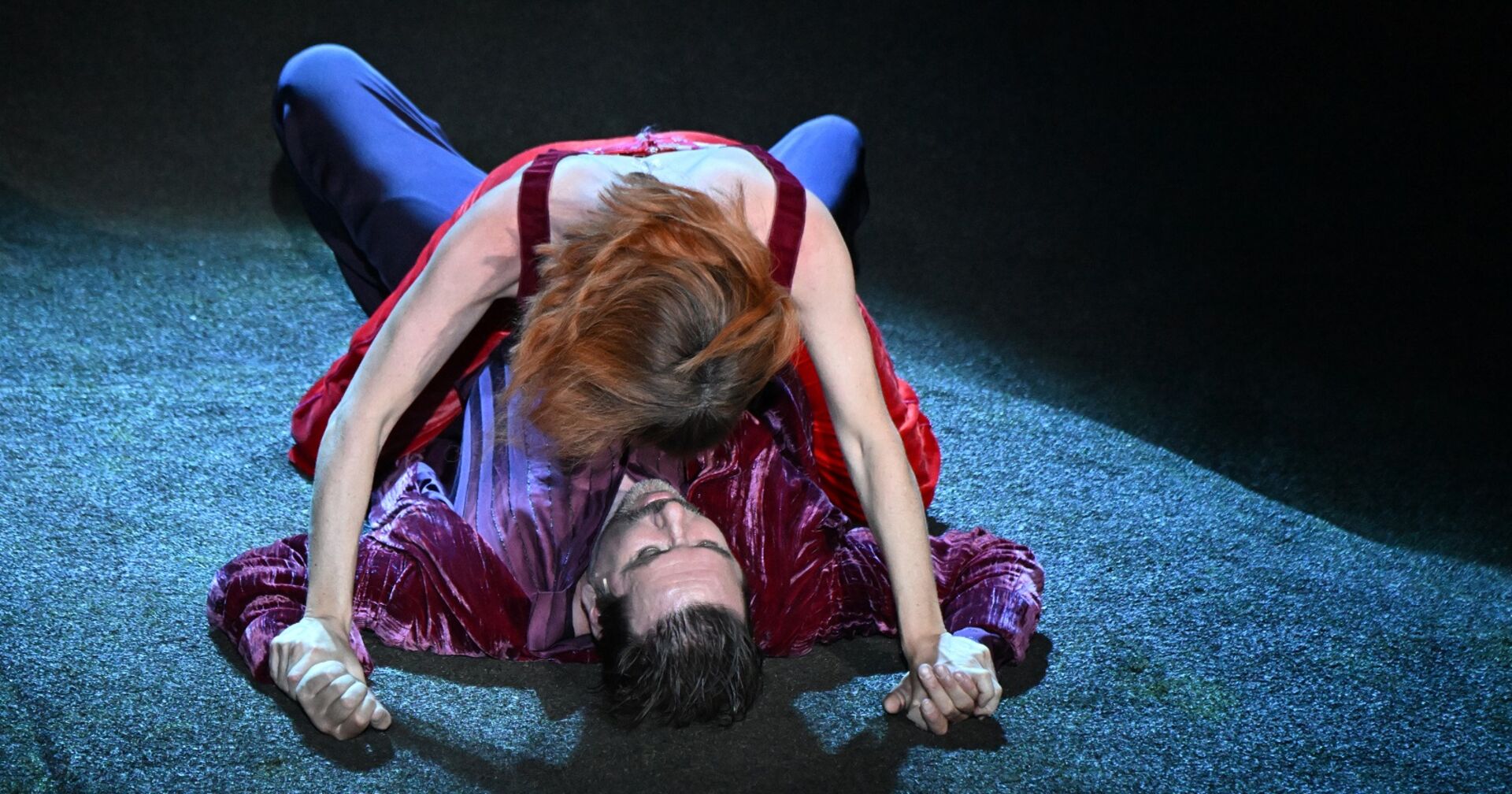 Die Buhlschaft kniet über dem liegenden Jedermann und hält ihn an den Händen fest.