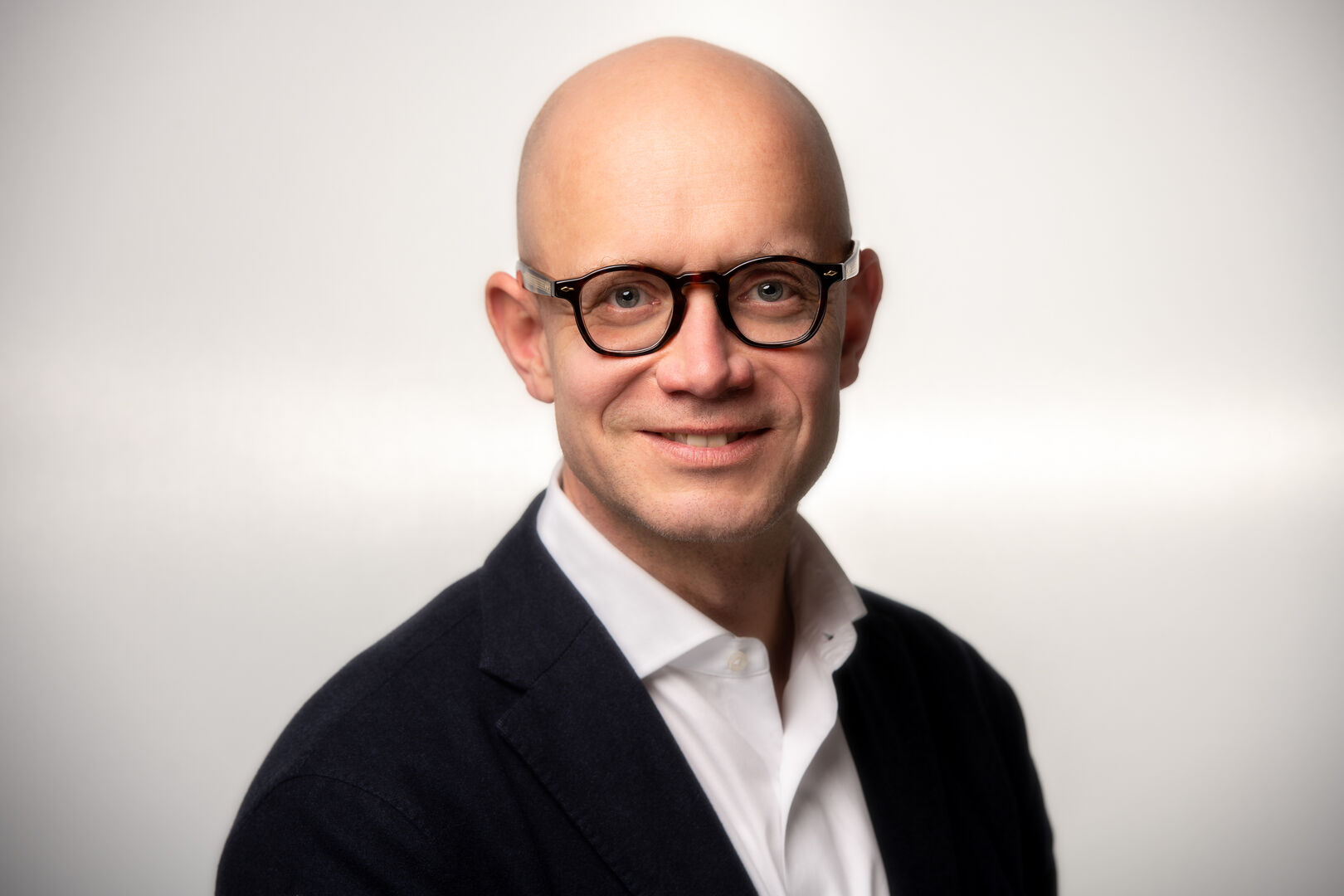 Porträtfoto von Peter Spak - ein Mann mit Glatze, der eine Brille sowie ein schwarzes Sakko samt weißem Hemd trägt