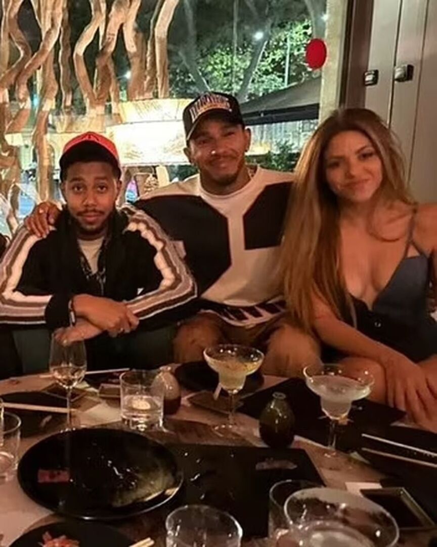 Lewis Hamilton sitzt mit Freunden an einem Tisch. Rechts von ihm sitzt Shakira in einem tief ausgeschnittenem Kleid, er hat den Arm um ihre Taille.