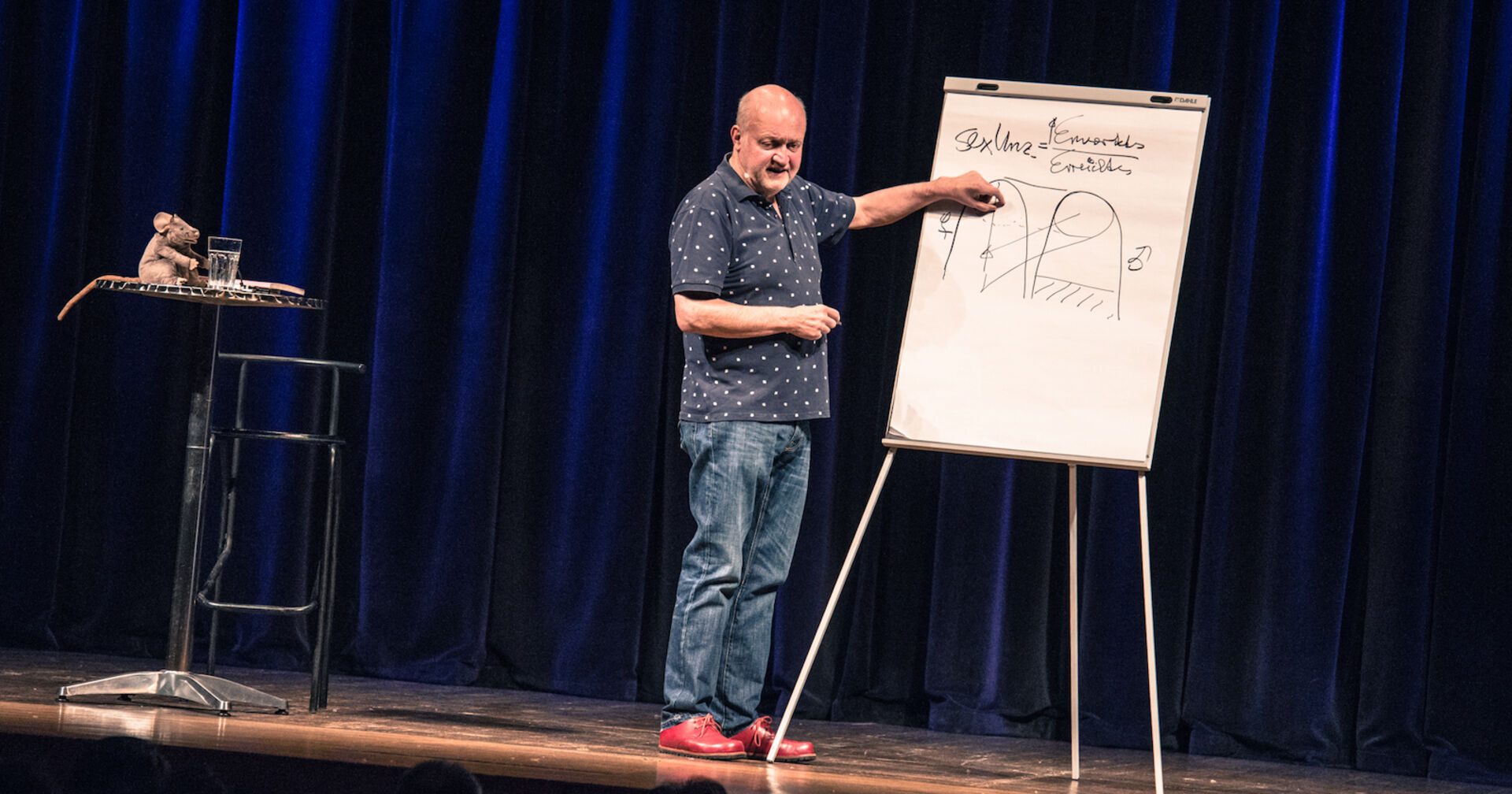 Bernhard Ludwig erklärt an einer Tafel auf der Bühne.