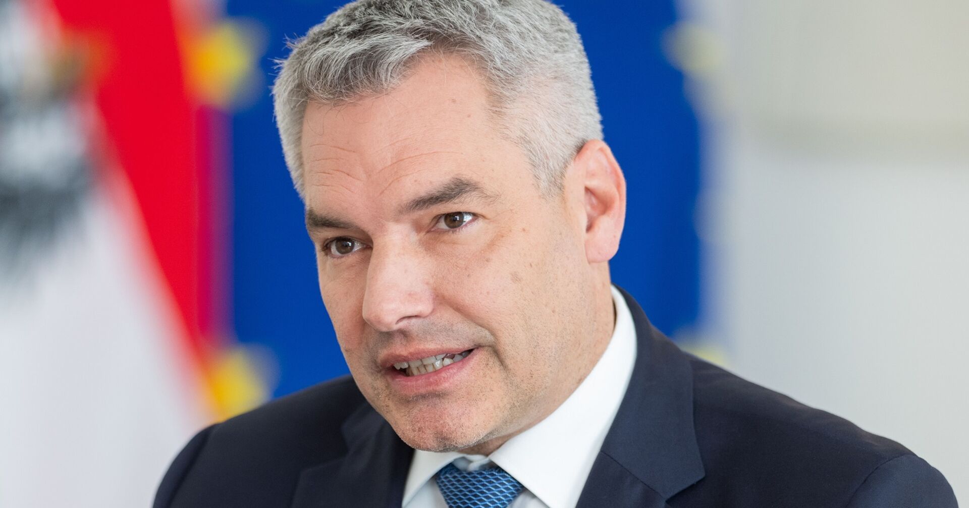 Kanzler Karl Nehammer im Porträt, hinter ihm eine Flagge der Europäischen Union