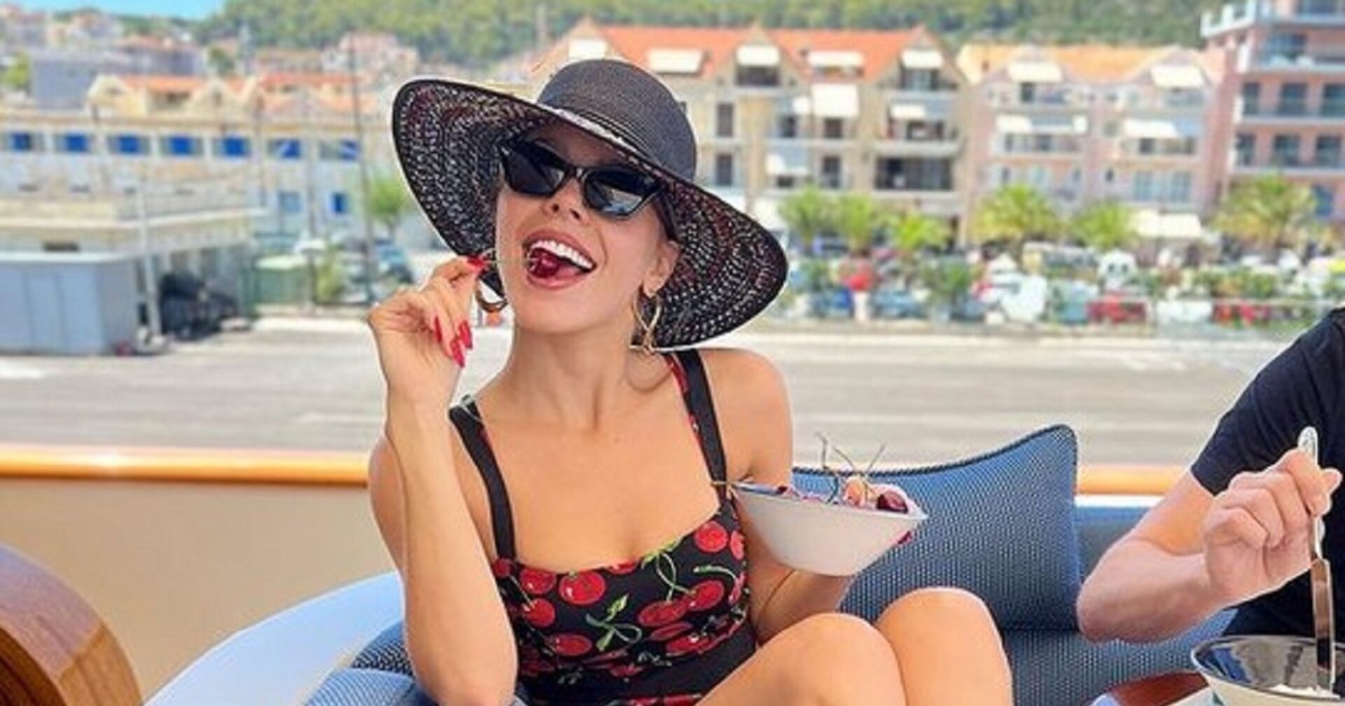 Victoria Swarovski mit Sonnenhut auf einer Yacht, sie isst eine Kirsche.