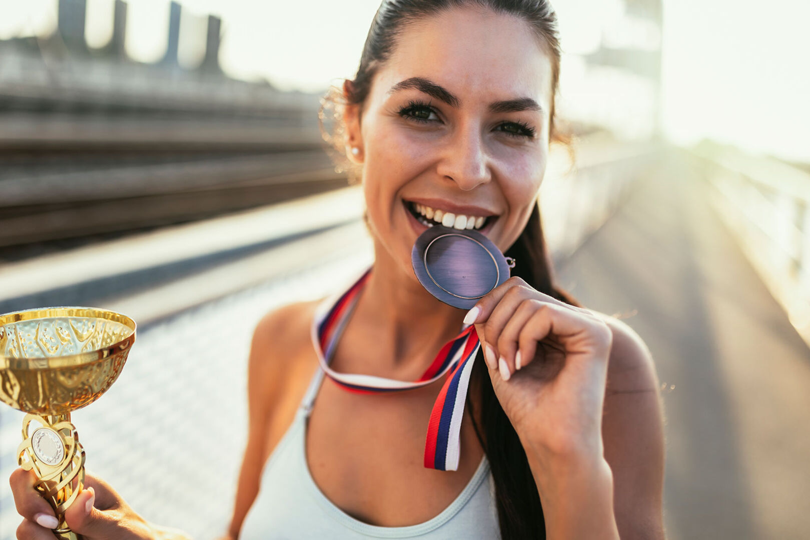 Läuferin mit Pokal und Medaille zwischen den Zähnen | Credit: iStock.com/Jovanmandic