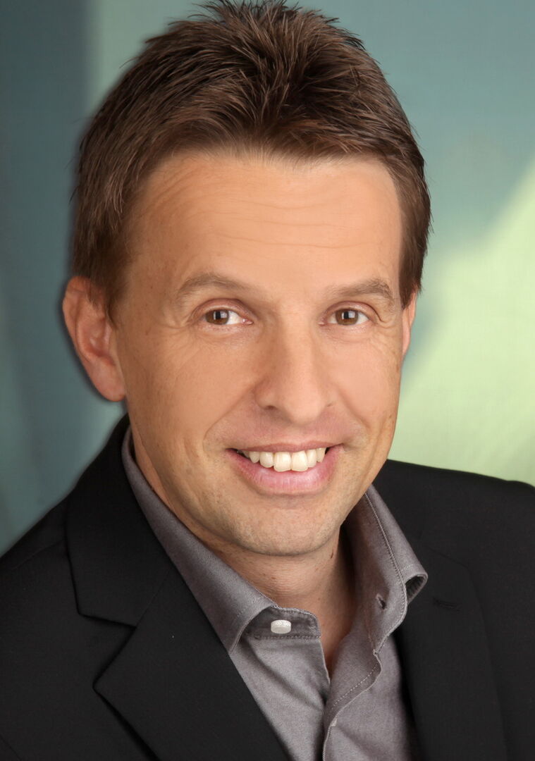 Porträtfoto von Enrik Mandl, der ein schwarzes Sakko mit grauem Hemd trägt