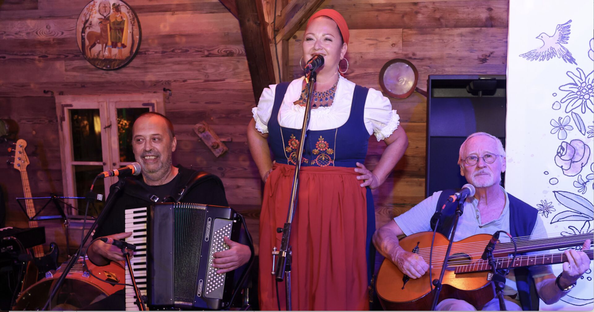 Akkordeon- und Gitarrenspieler sitzend, dazwischen stehend die Sängerin