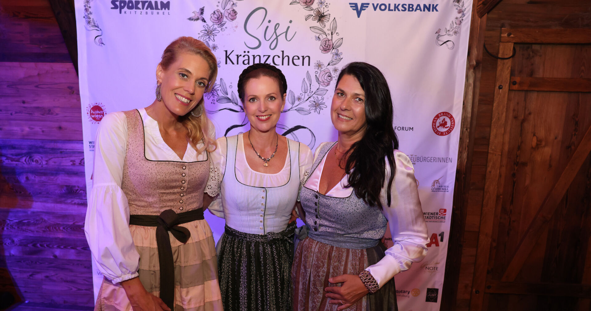 Drei Frauen im Dirndl vor einem Banner mit Sponsorenlogos und dem Schriftzug &quot;Sisi Kränzchen&quot;