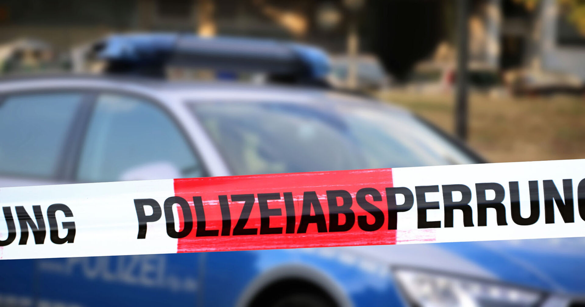 Themenbild: Polizeiabsperrung mit Polizeiauto im Hintergrund