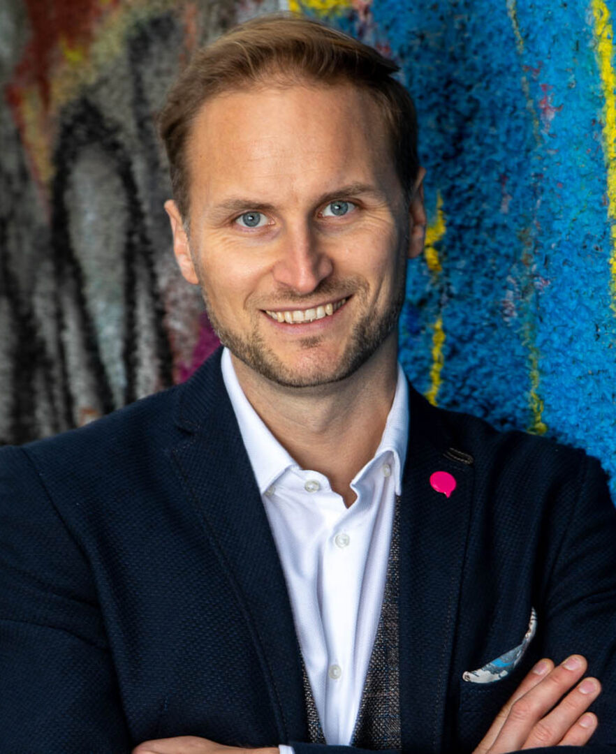 Porträtfoto von Janos Juvan, der ein Sakko samt weißem Hemd sowie einen NEOS-Button auf dem Revers trägt