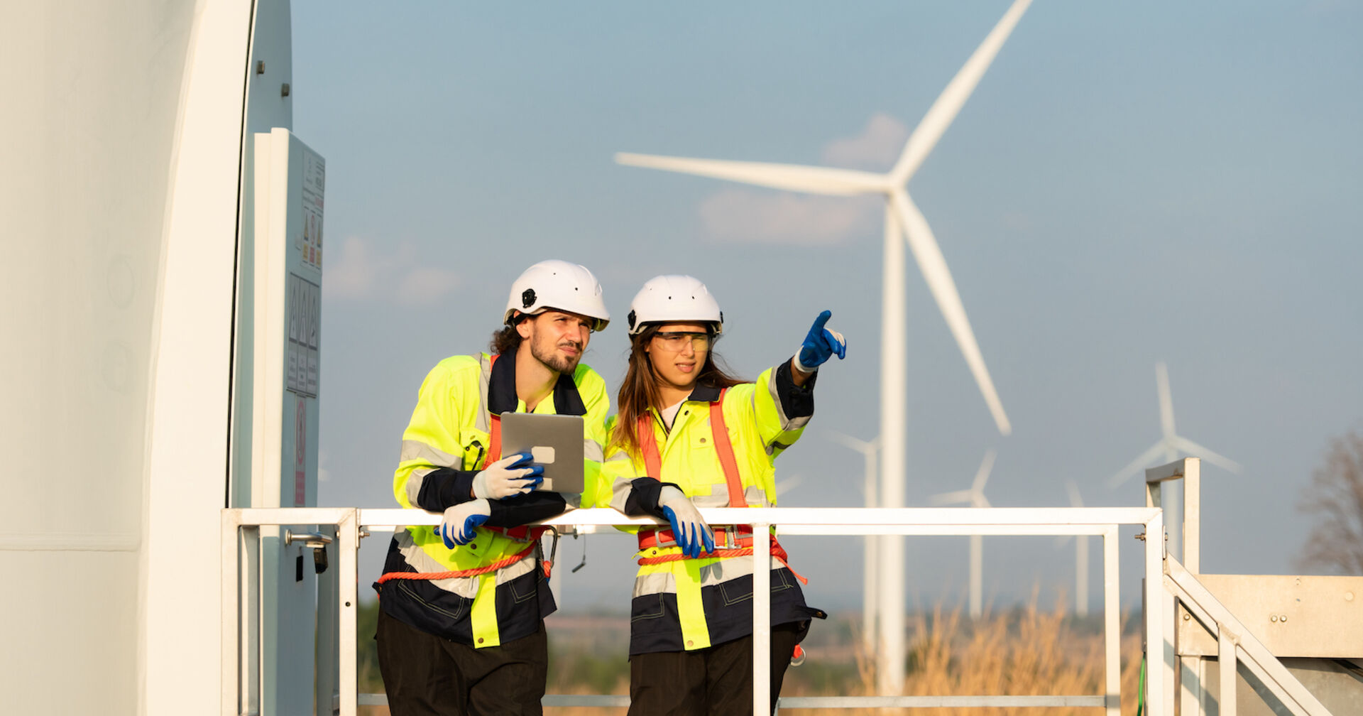 Zwei Arbeiter stehen in einem Windrad-Park und inspizieren dieses
