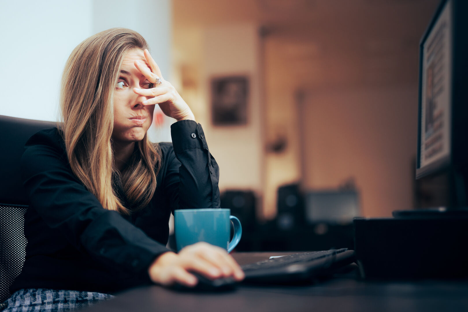 Eine junge Frau bedeckt ihre Augen teilweise mit ihrer Hand, während sie einen schockierten Blick auf einen Computerbildschirm wirft