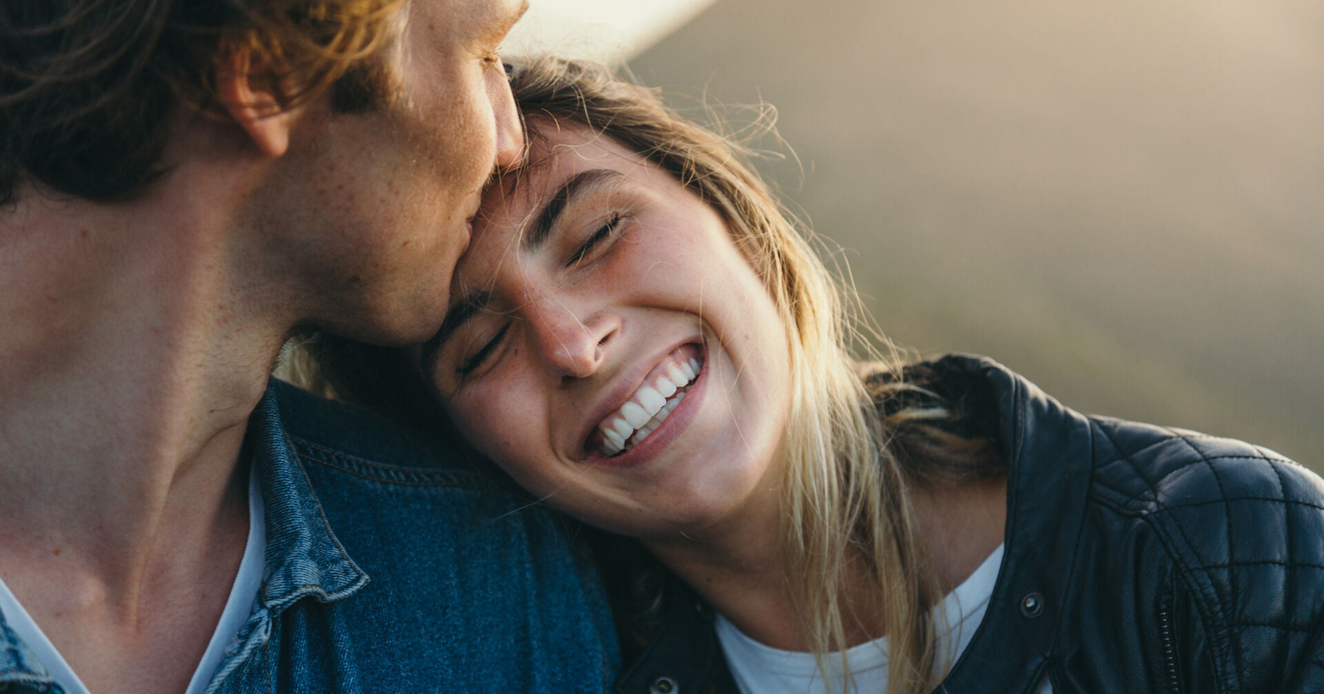 Ein Mann gibt einer Frau einen Kuss auf die Stirn. Sie lacht ihn verliebt an.