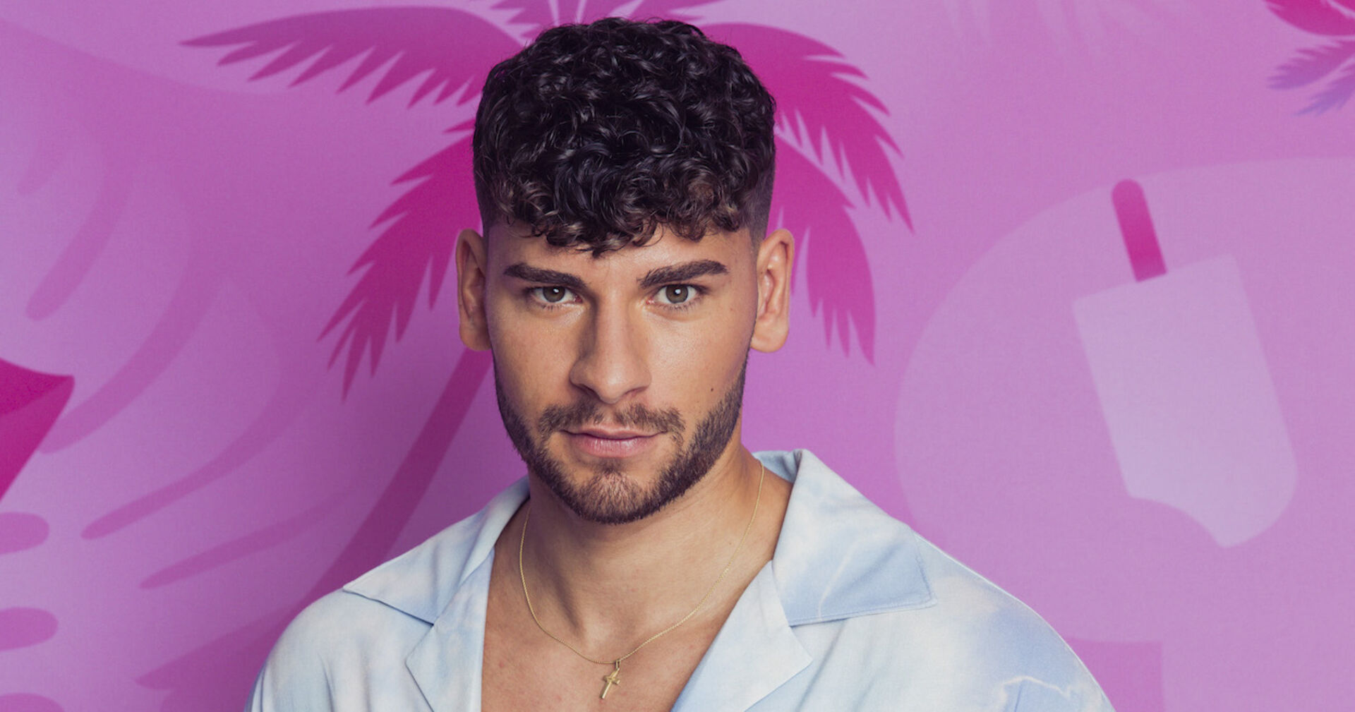 Kandidat Fabi vor der pinken Love Island Wand mit braunen kurzen Haare und einem hellblauen Hemd.