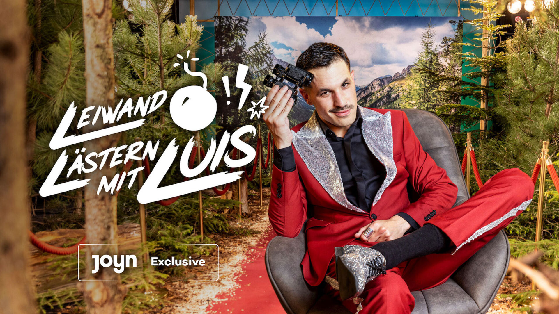 Mann in rotem Anzug vor einer Waldleinwand.