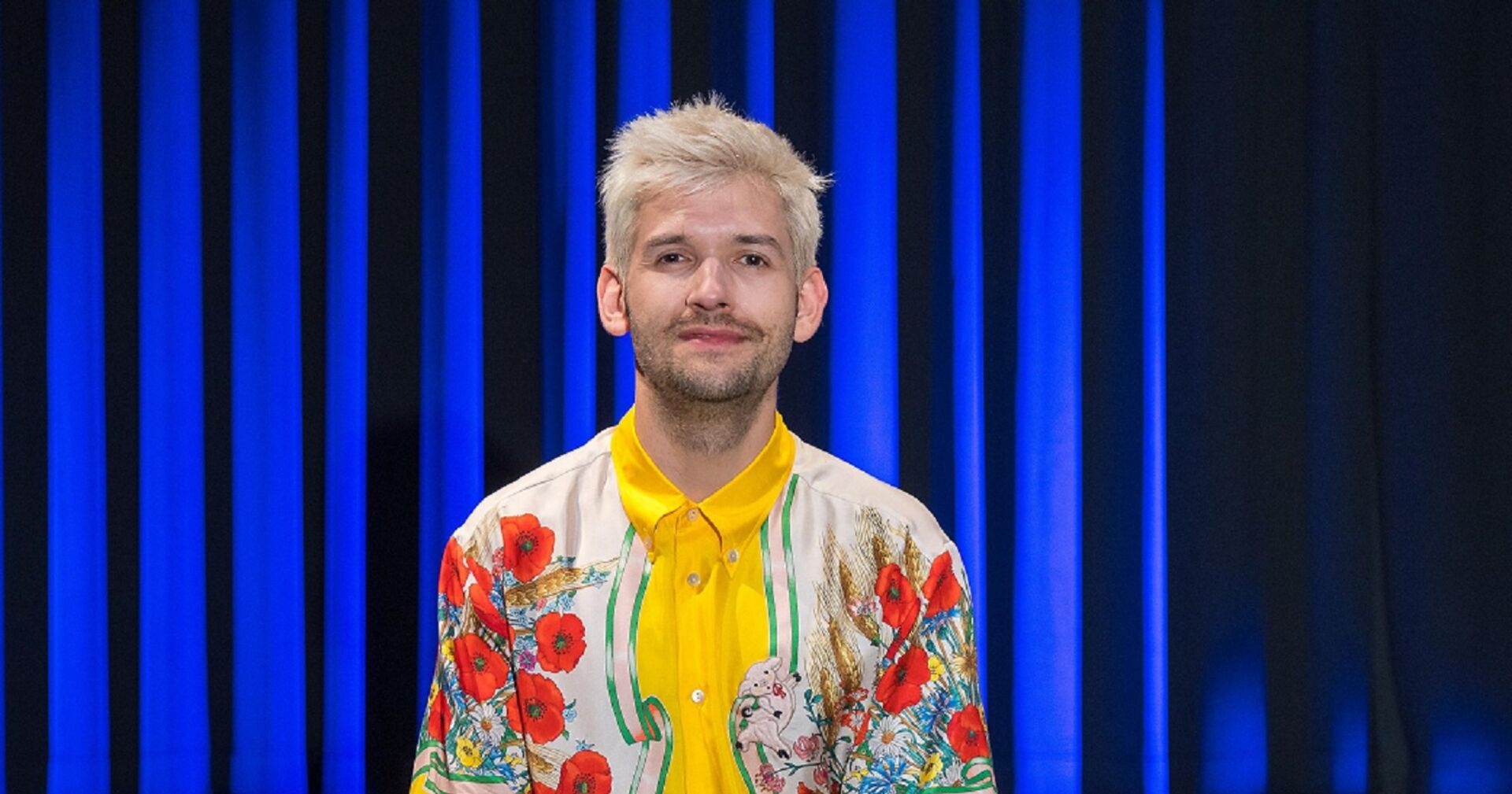 Michael Buchinger in einem bunten Kostüm auf der Kabarettbühne.