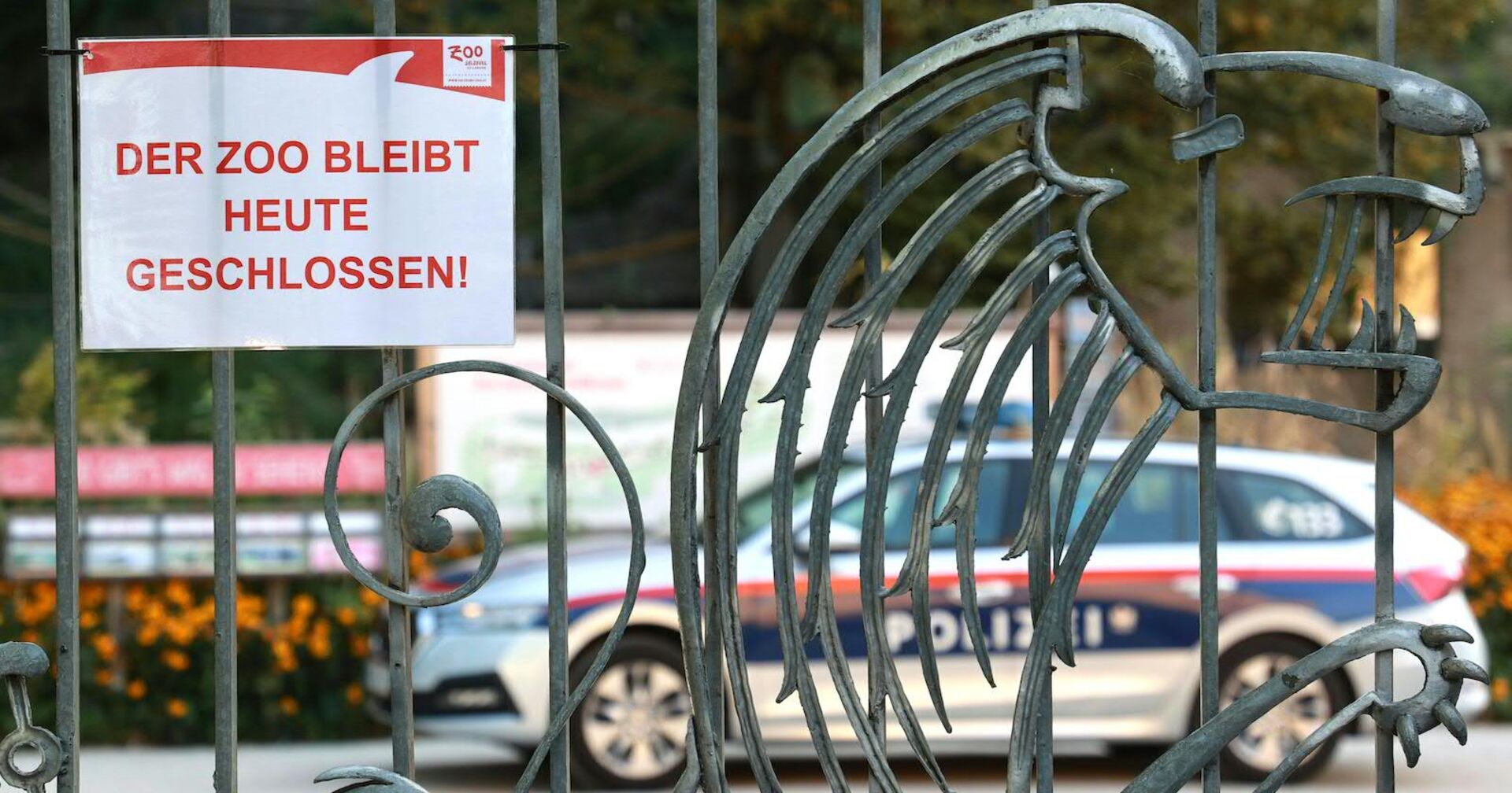 Das Eingangstor des Zoos, darauf die Info: &quot;Der Zoo bleibt heute geschlossen!&quot; Im Inneren der Anlage ist ein Polizeiauto geparkt.