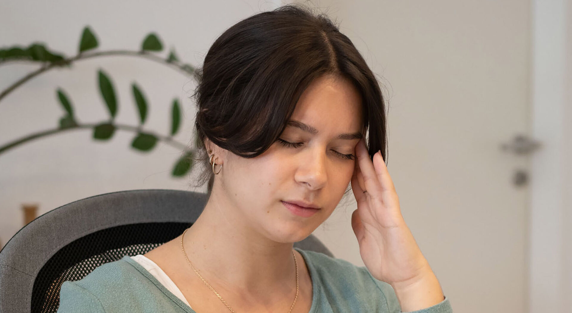 Frau mit Hand an der Schlefe und braunen Haaren die über Schmerzen klagt.