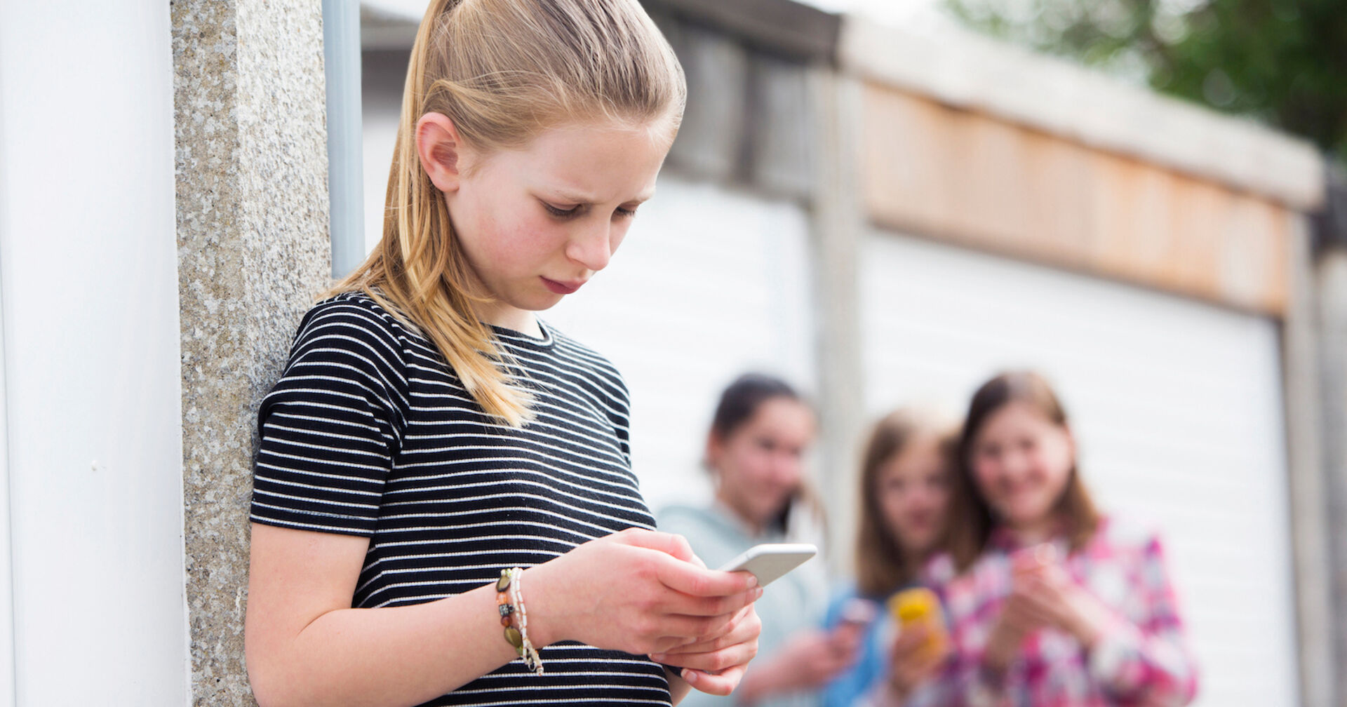 Mädchen schaut traurig in ihr Handy, dahinter stehen lachende Mädchen