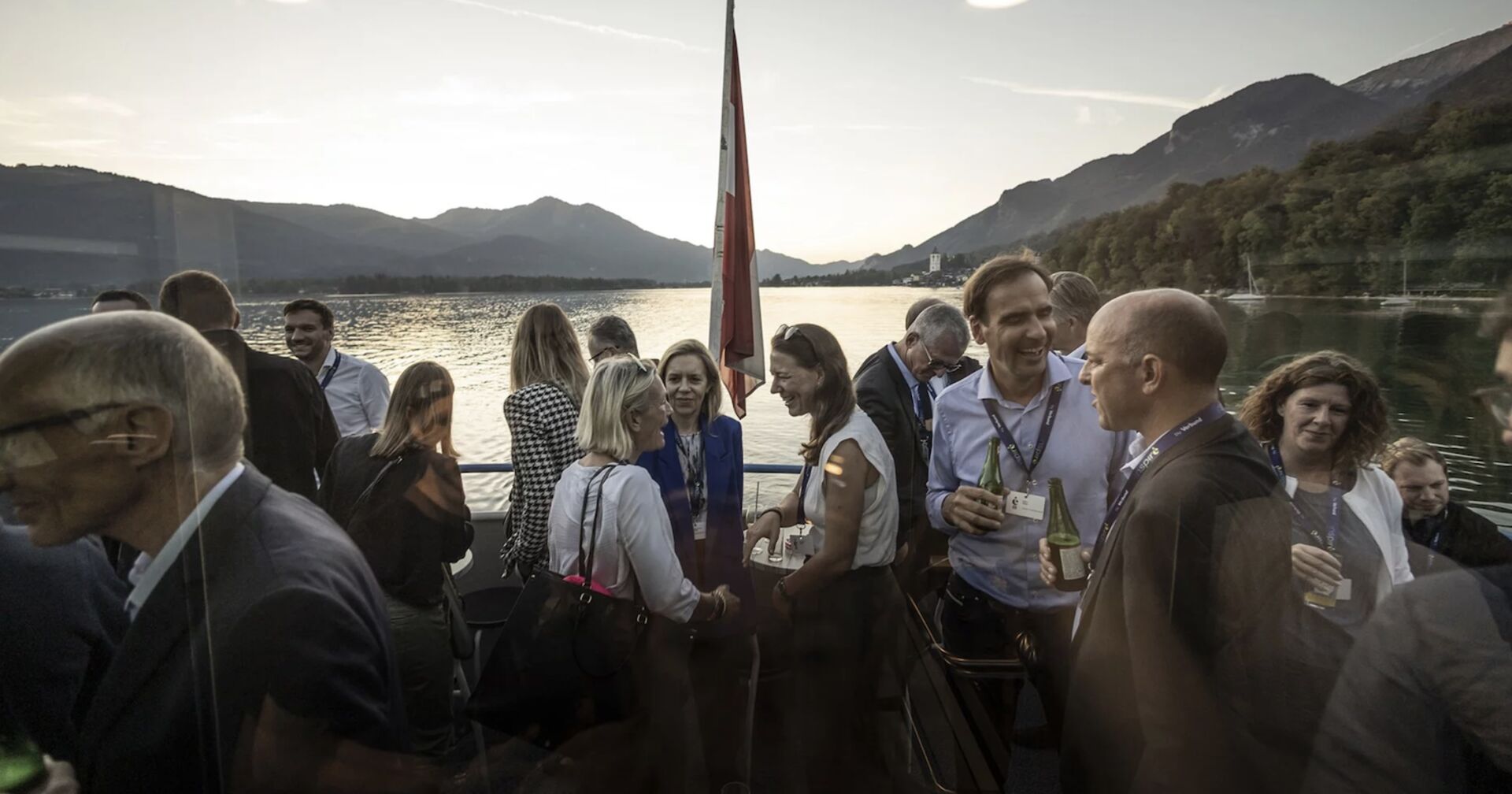 Grüppchen stehen am Schiffsdeck, im Hintergrund See und Berge