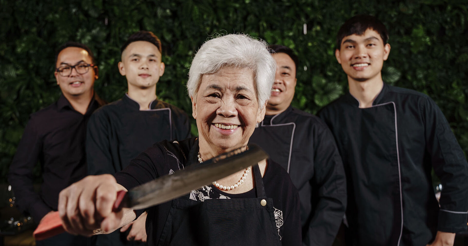 Ein fröhliches Gruppenfoto zeigt eine ältere Frau in der Mitte, umgeben von vier jüngeren Männern.