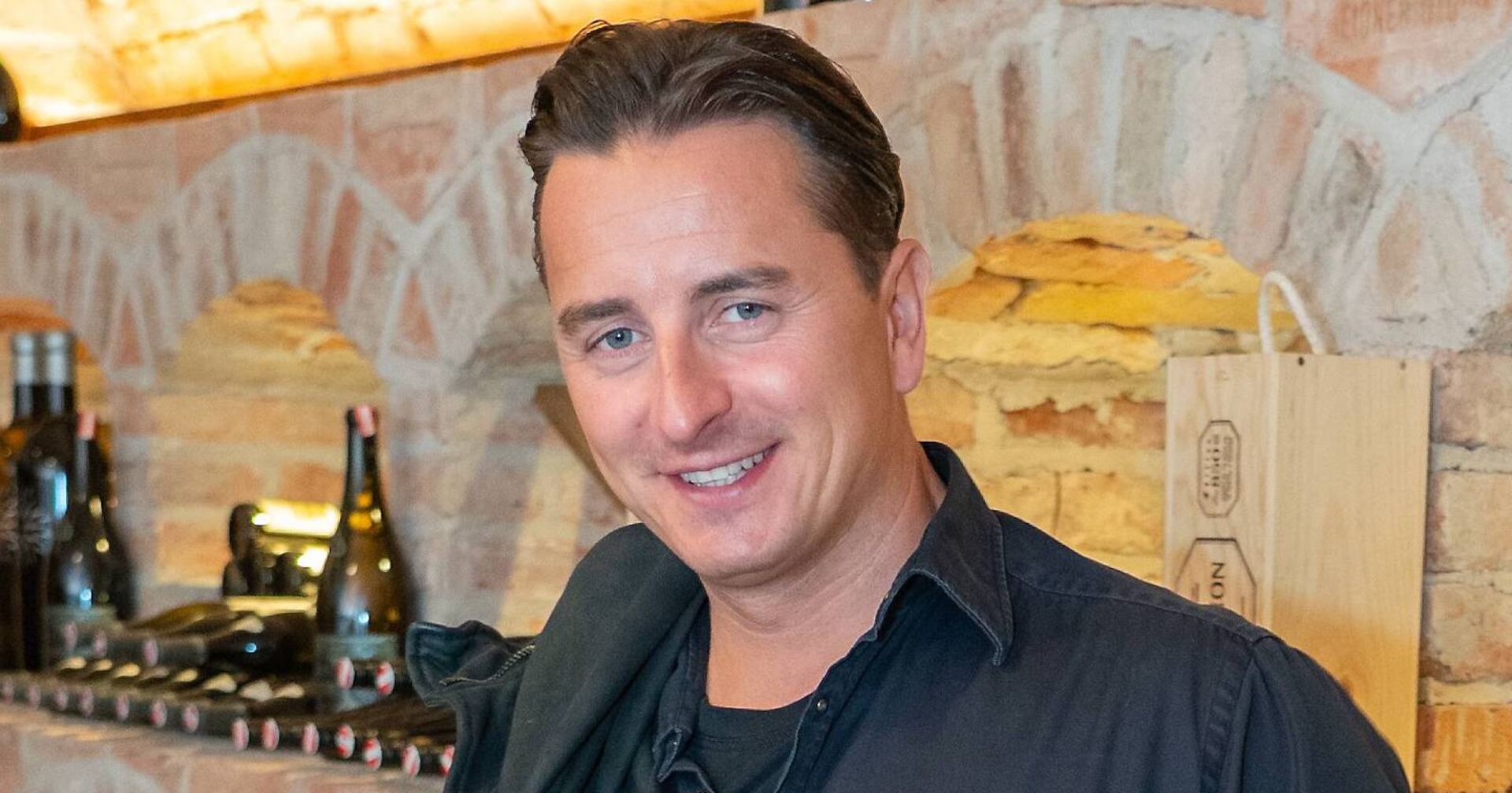 Andreas Gabalier steht in einem Weinkeller vor einem Weinregal.
