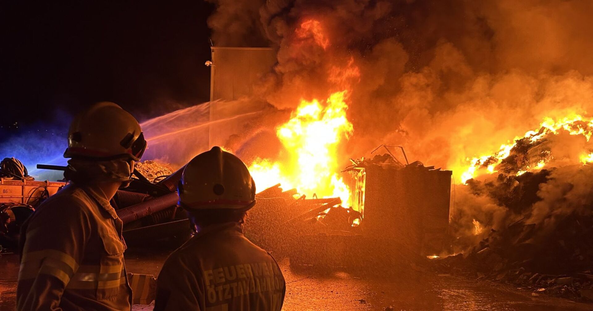 Zwei Feuerwehrleute blicken in die Flammen.