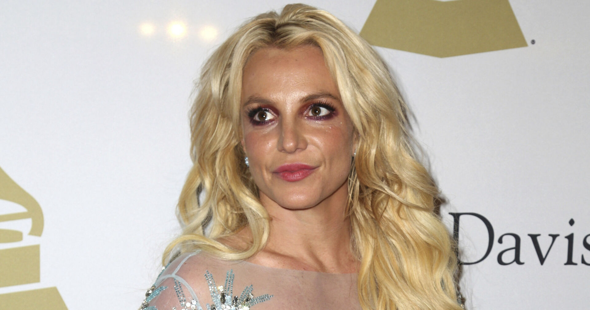 Britney Spears vor einer Fotowand mit offenen blonden Haaren und einem silbernen Kleid.