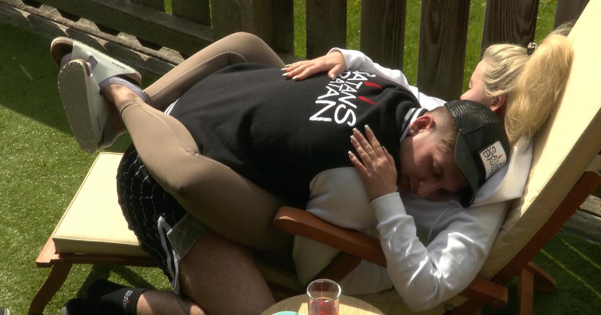 Der Influencer Satans Bratan liegt auf einer Liege zwischen den Beinen von Cathy Lugner.