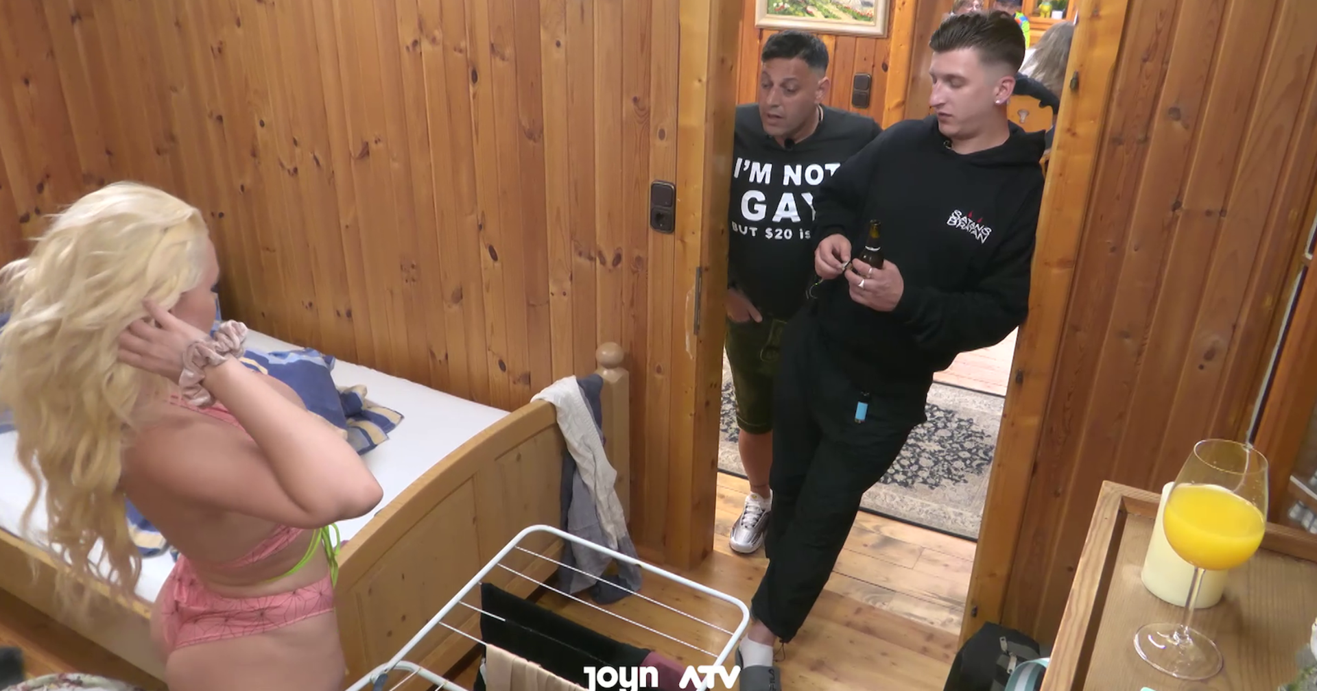 Im Forsthaus Rampensau steht eine blonde Dame namens Miss Jackson im Bikini vor einem Comedian und einem anderen Showteilnehmern. Sie trägt einen pinken Bikini und die Herren einen schwarzen Jogginganzug.