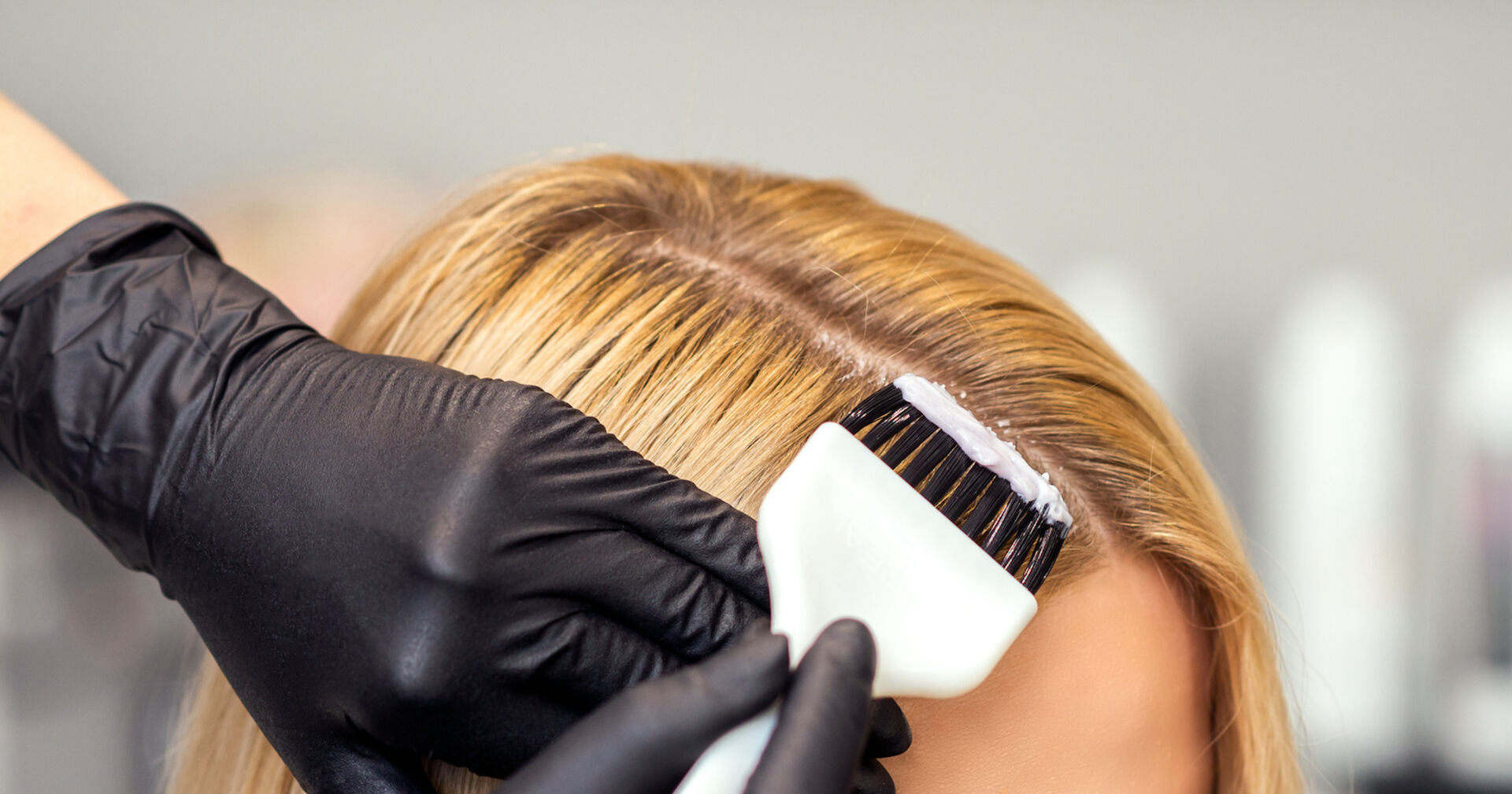 Der dunkle Ansatz eines blonden Haarschopfes wird nachgefärbt.