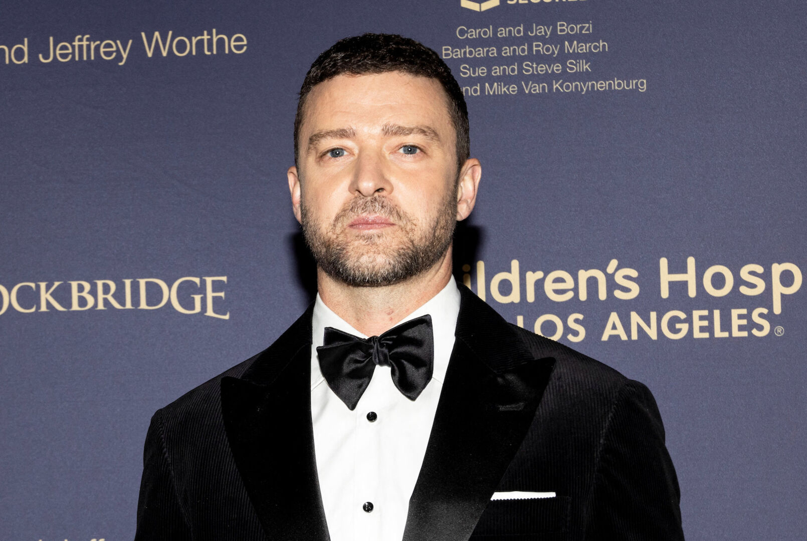 Justin Timberlake trägt einen schwarzen Suite und kurze Haare vor einer Fotoleinwand.
