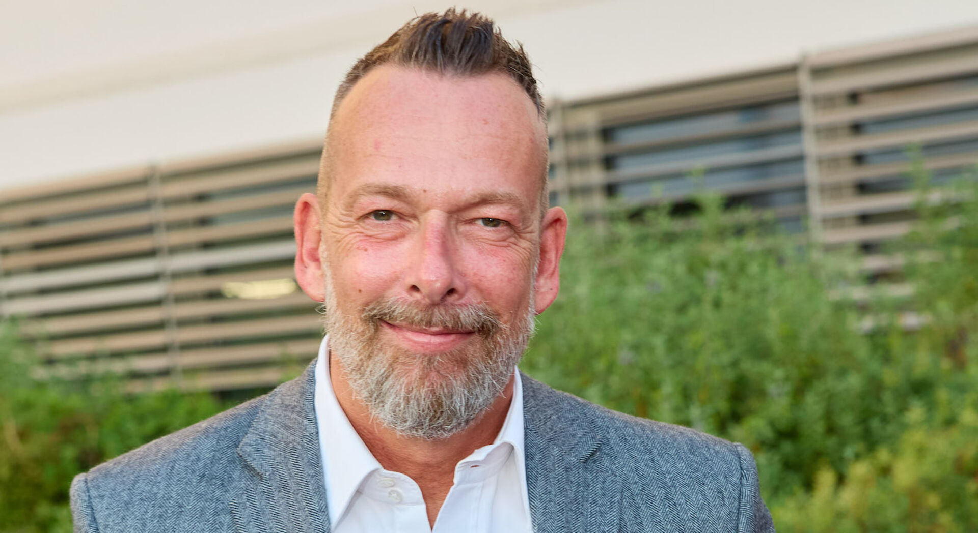 Robert Kratky aufgestellten Haaren in einem blauen Anzug vor einem Gebäude