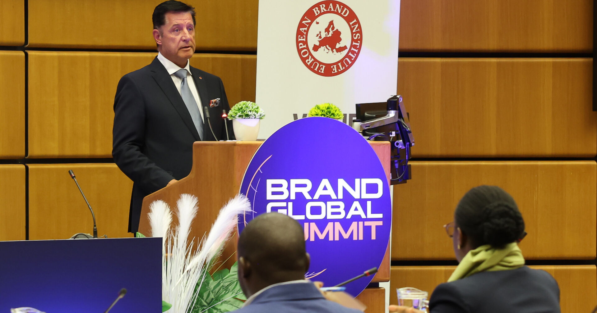 Porträt am Rednerpult vor Logos