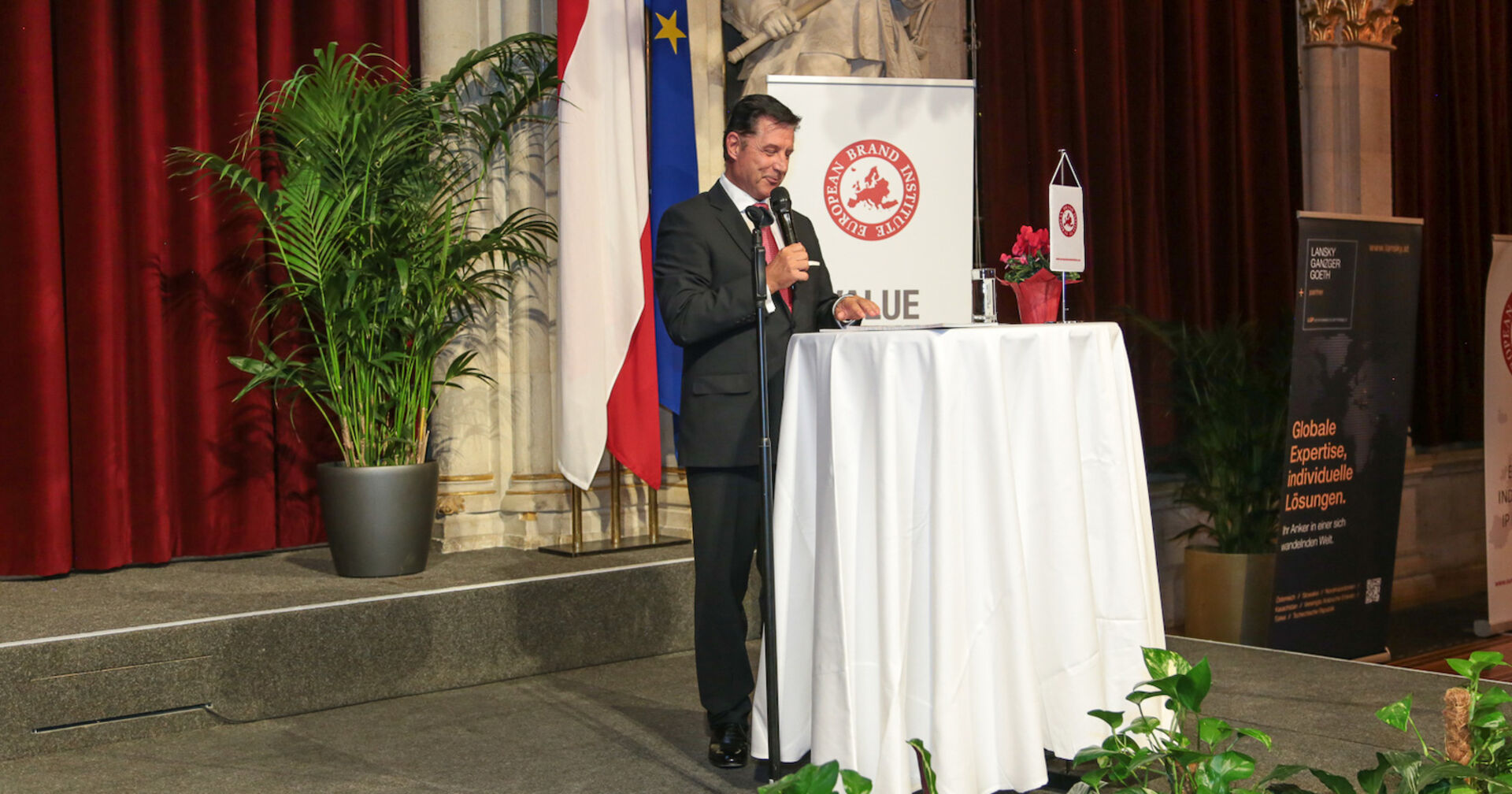 Redner vor rundem Tischchen mit bodenlanger Tischdecke