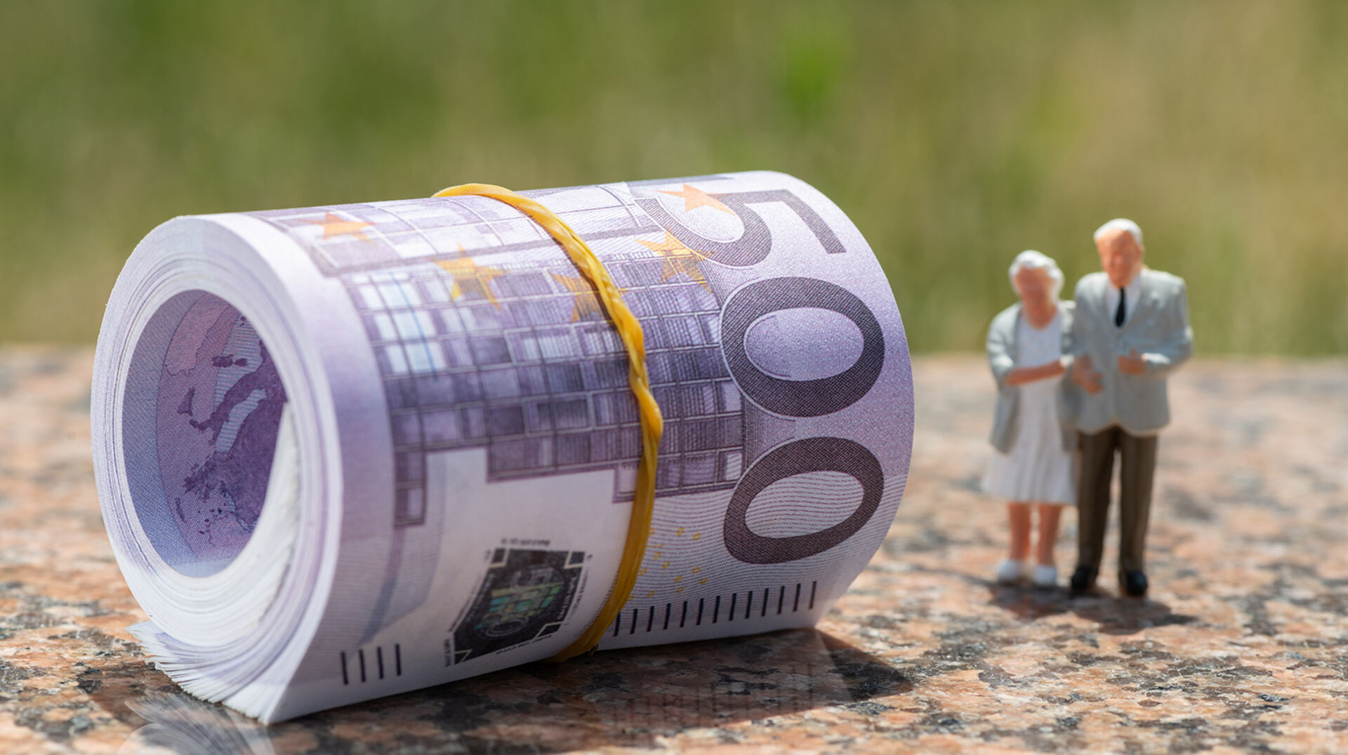 Ein Bündel von 500 Euro-Scheinen neben einer Miniaturausgabe eines Senioren-Paares | Credit: iStock.com/Max Zolotukhin