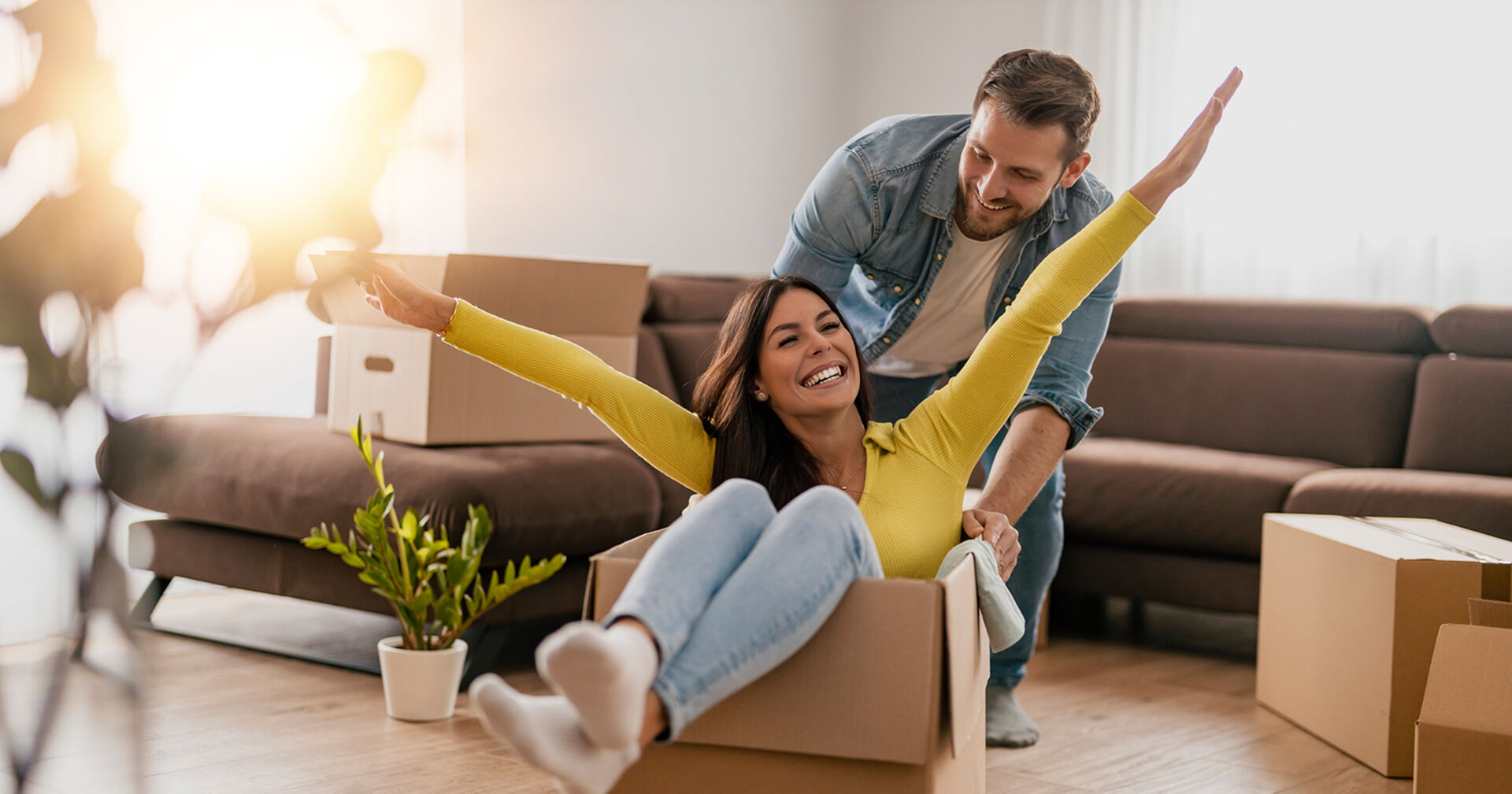 Mann schiebt seine Freundin im Umzugskarton durch das Wohnzimmer | Credit: iStock.com/Ivanko_Brnjakovic