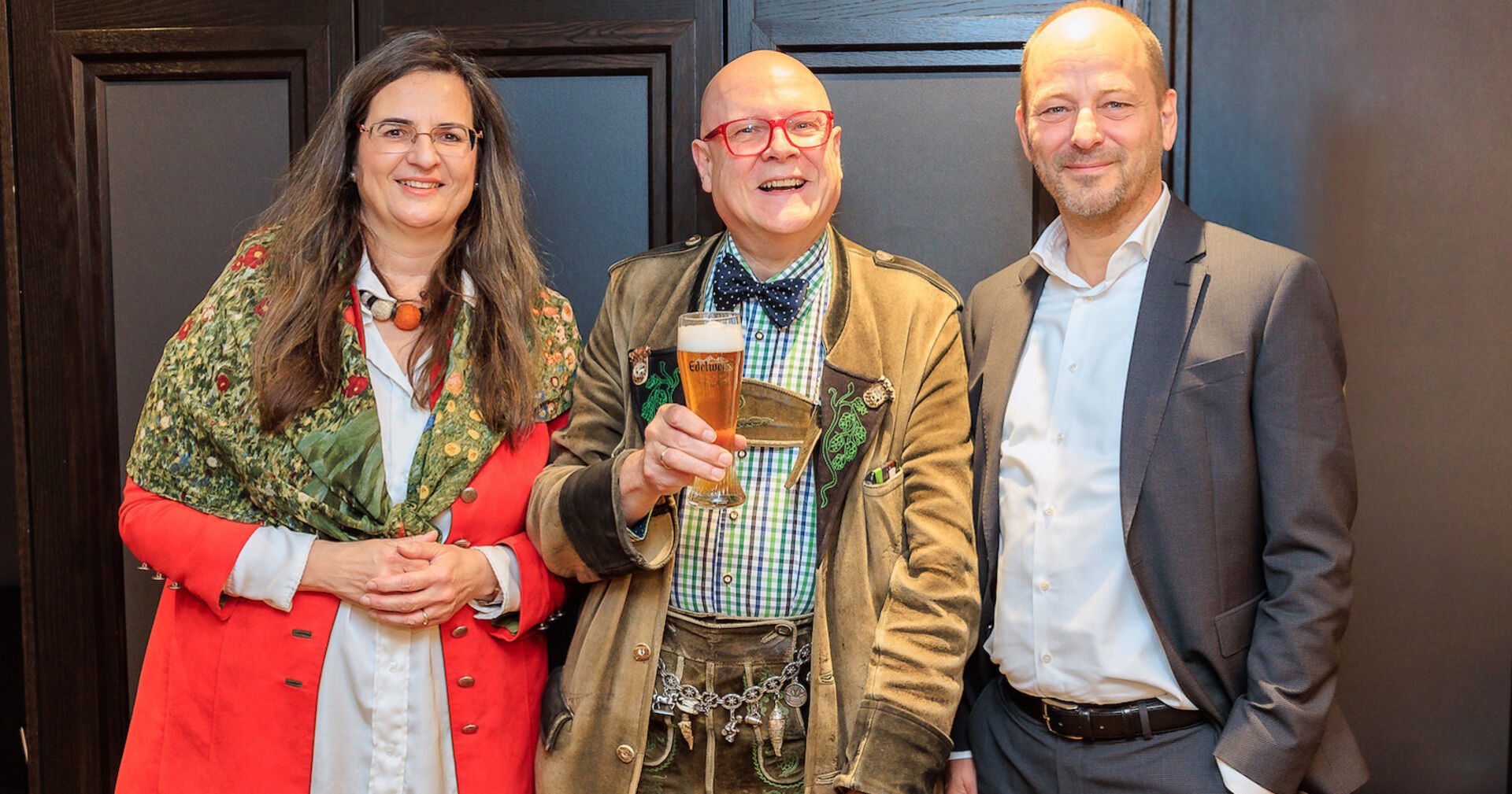 Drei Personen nebeneinander, der mittlere hält ein Bierglas in der Hand