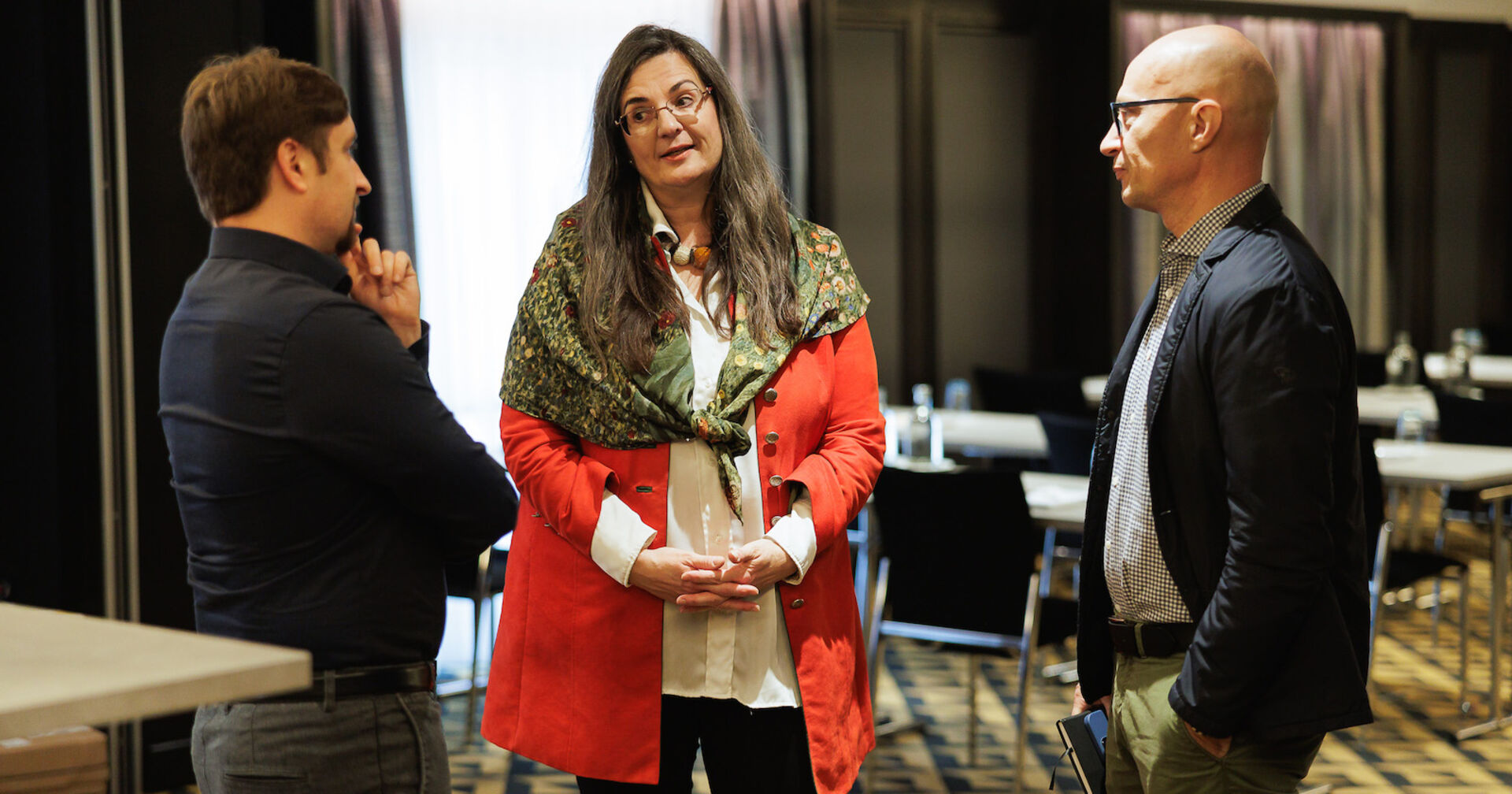 In der Mitte eine Frau, links und rechts hören zwei Männer zu