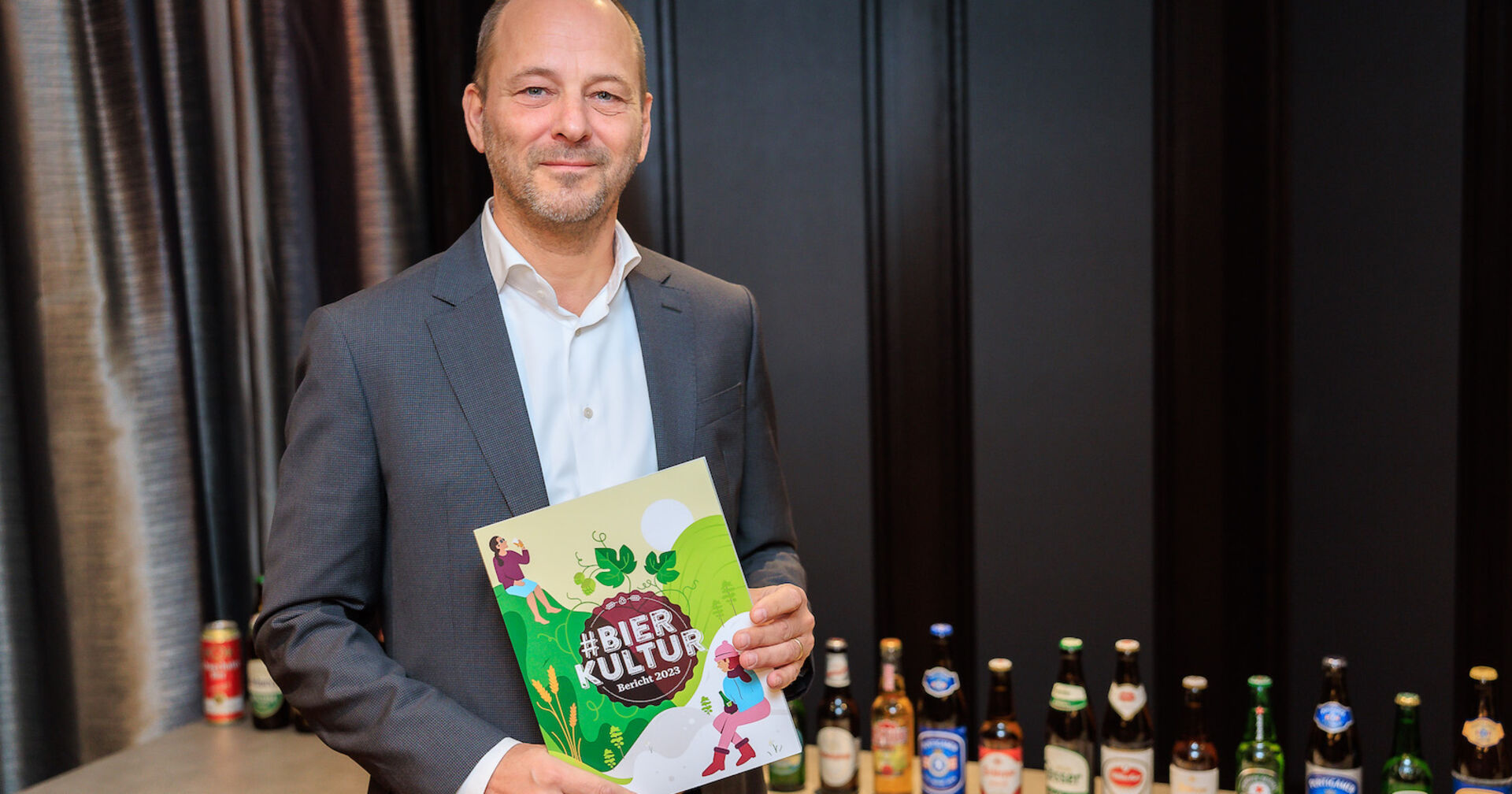 Porträt mit Bierkulturbericht in den Händen, im Hintergrund Bierflaschen