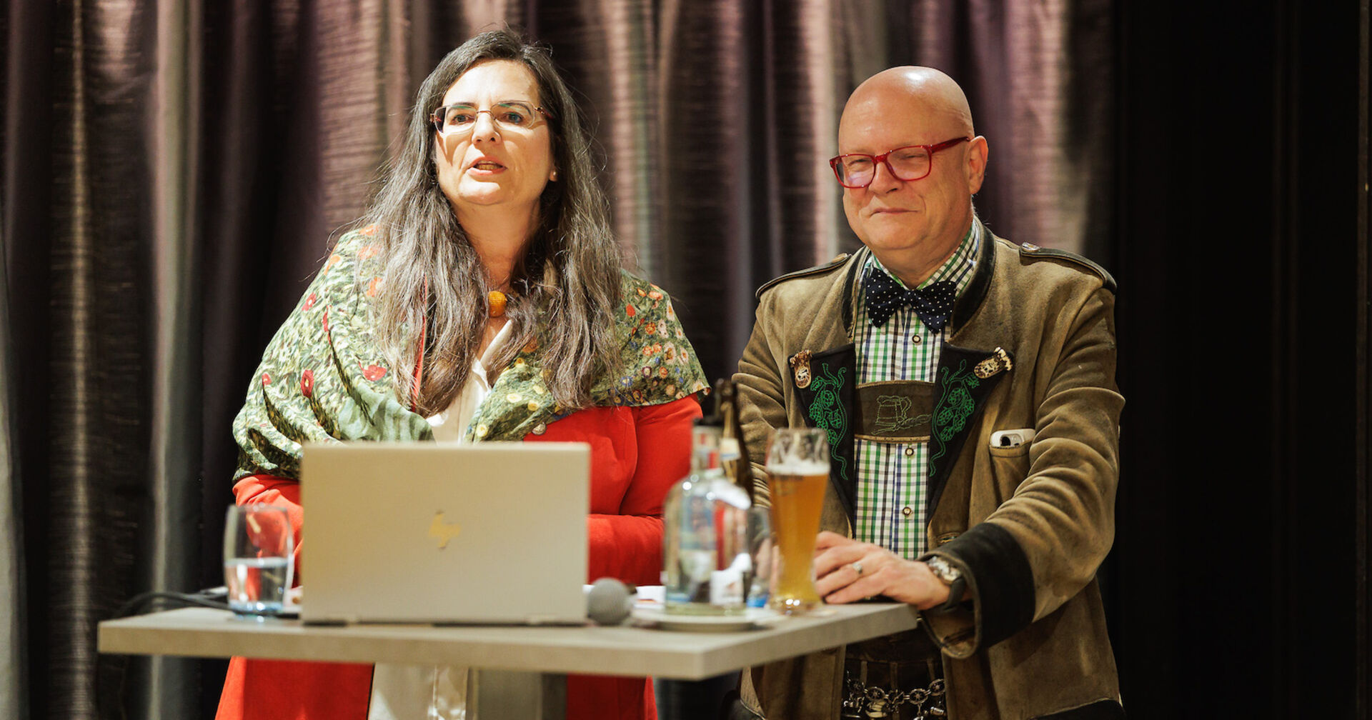 Zwei Personen am Rednerpult mit aufgeklapptem Laptop