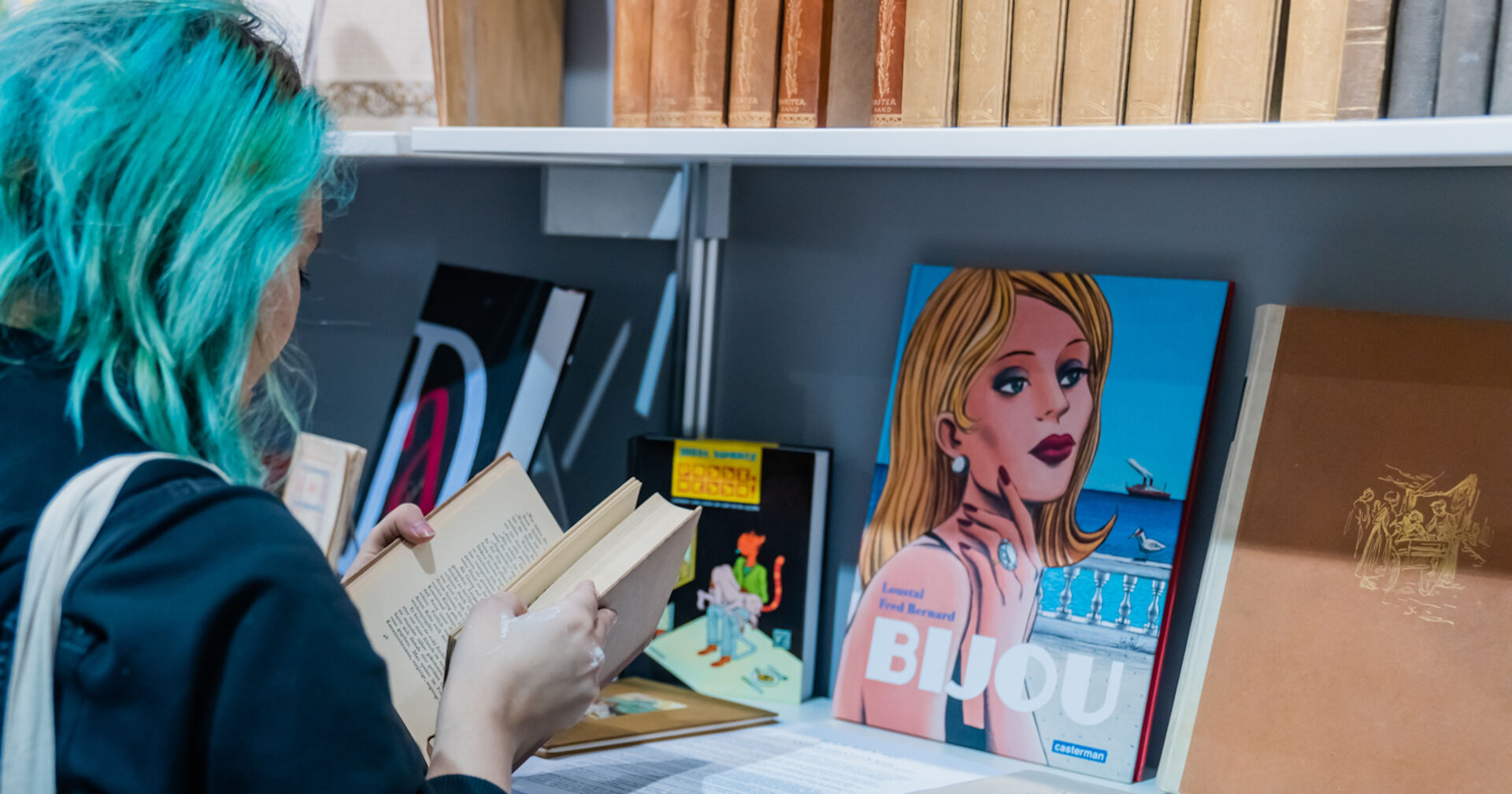 Junge Frau mit blauen Haaren in einem Buch blätternd, von hinten