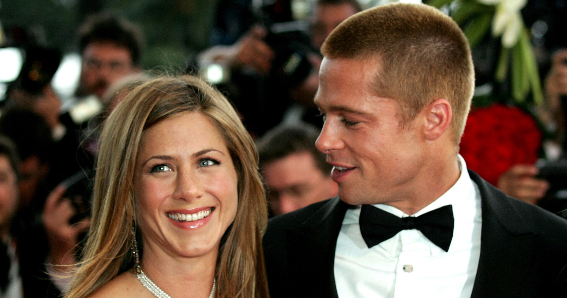 Brad Pitt und Jennifer Aniston. Sie hat offene blonde Haare und er trägt einen Smoking mit einer schwarzen Fliege.