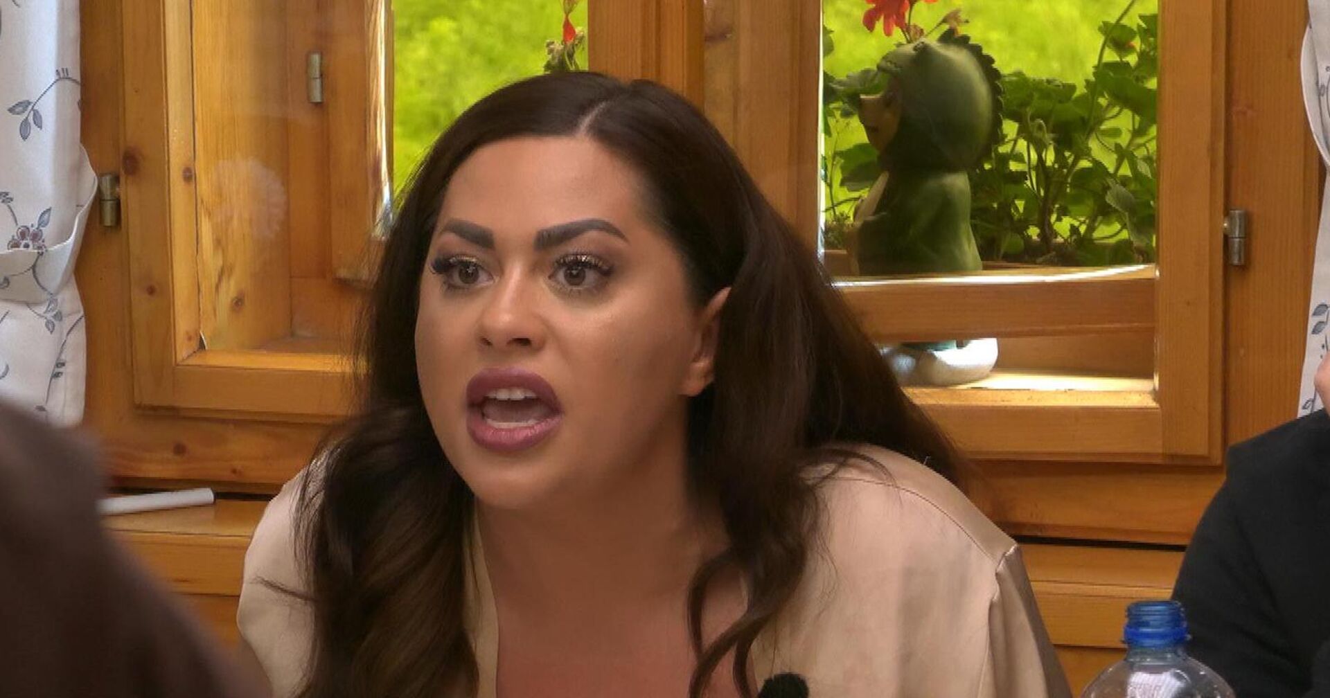 Costina hat eine erzürnte Mimik und lange brünette Haare. Sie trägt ein Cremefarbenes Satinoberteil.