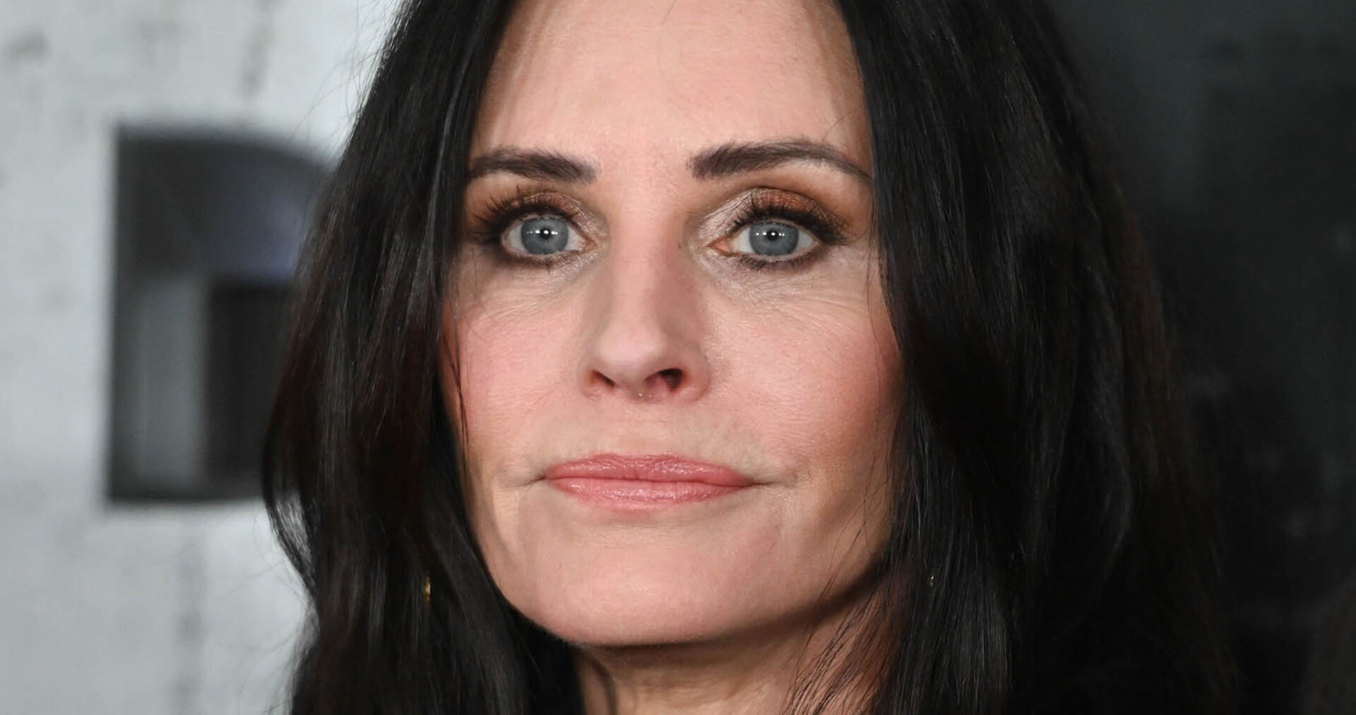 Courtney Cox blickt nachdenklich in die Ferne. Sie hat offene schwarze Haare und dunkel geschminkte Augen.