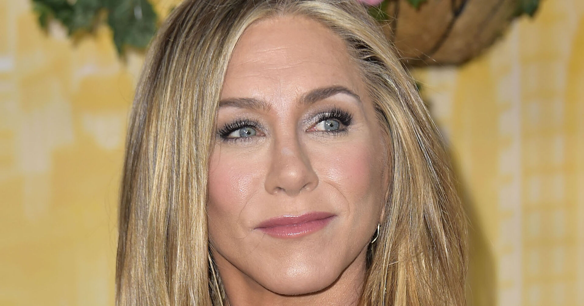 Jennifer Aniston trägt offene blonde Haare und hat ein schimmerndes Augen Make-Up. Sie schaut in die Ferne.