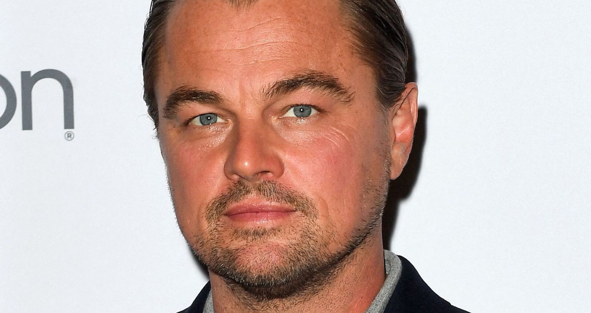 Leonardo DiCaprio steht vor einer weißen Fotoleinwand.