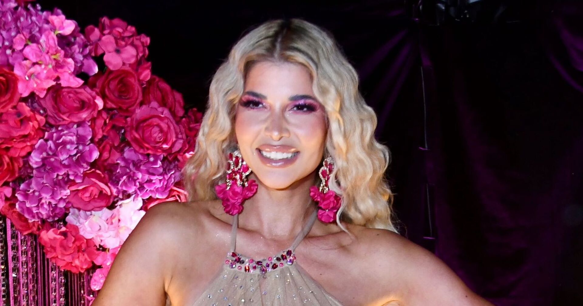 Micaela Schäfer mit offenen blonden Haaren vor einer Wand aus Rosen.